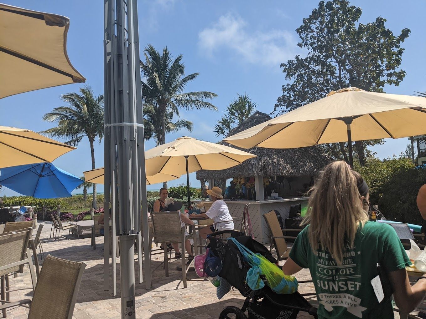 A group of people are sitting under umbrellas at a beach restaurant.