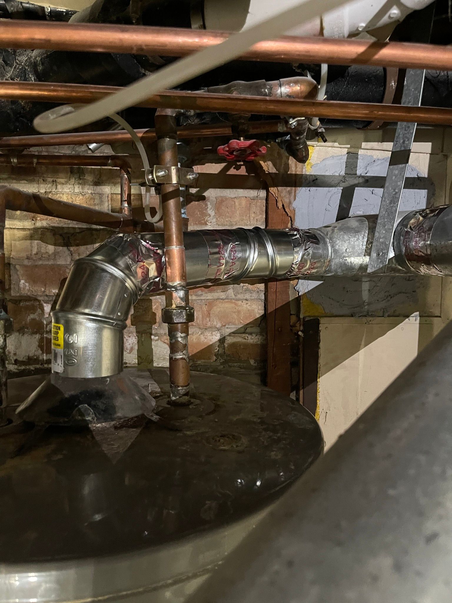 Plumbing with copper pipes and a black tank against a brick wall.