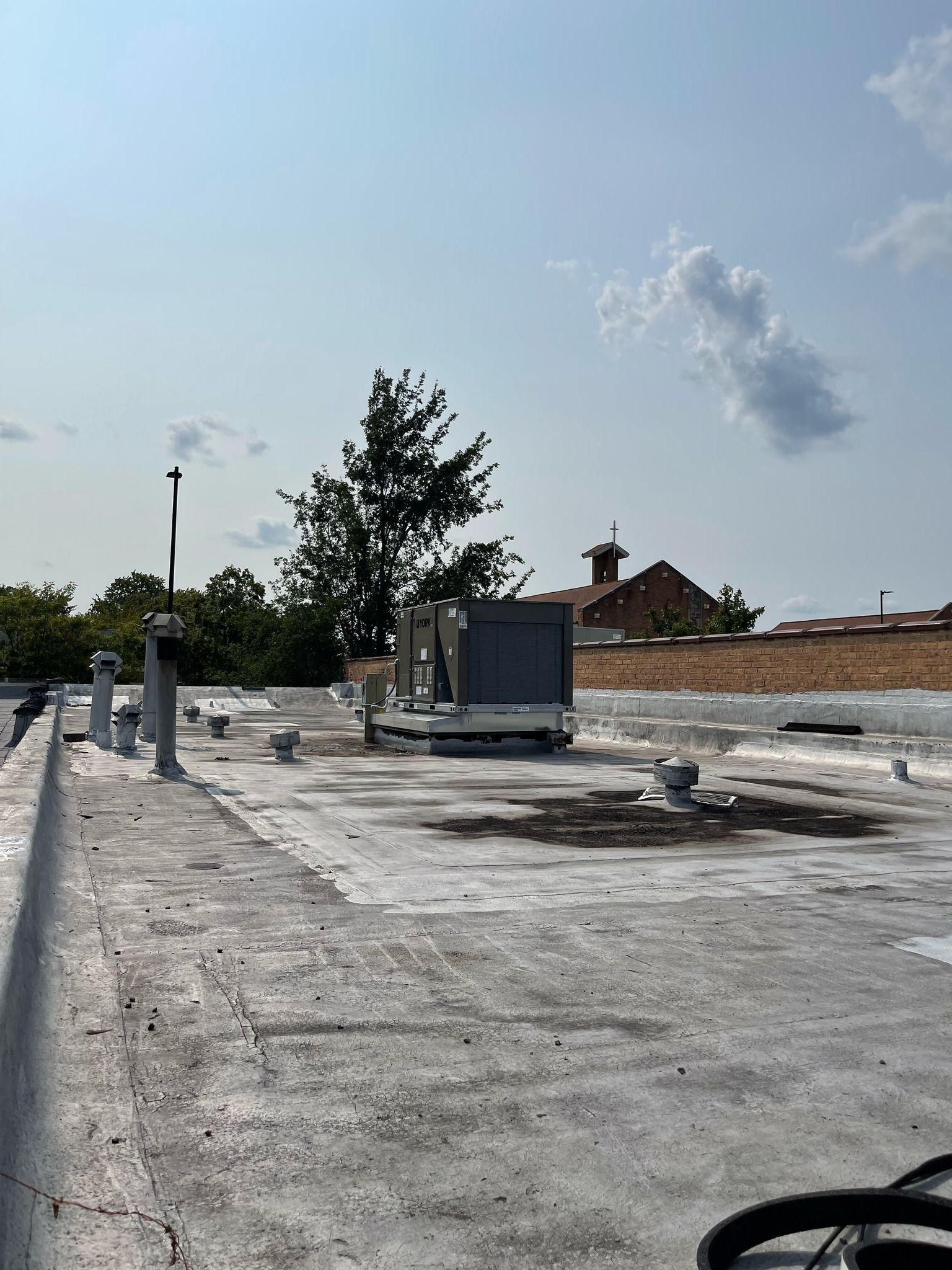 Gray rooftop with HVAC unit, antennas, and a tree; blue sky with clouds.