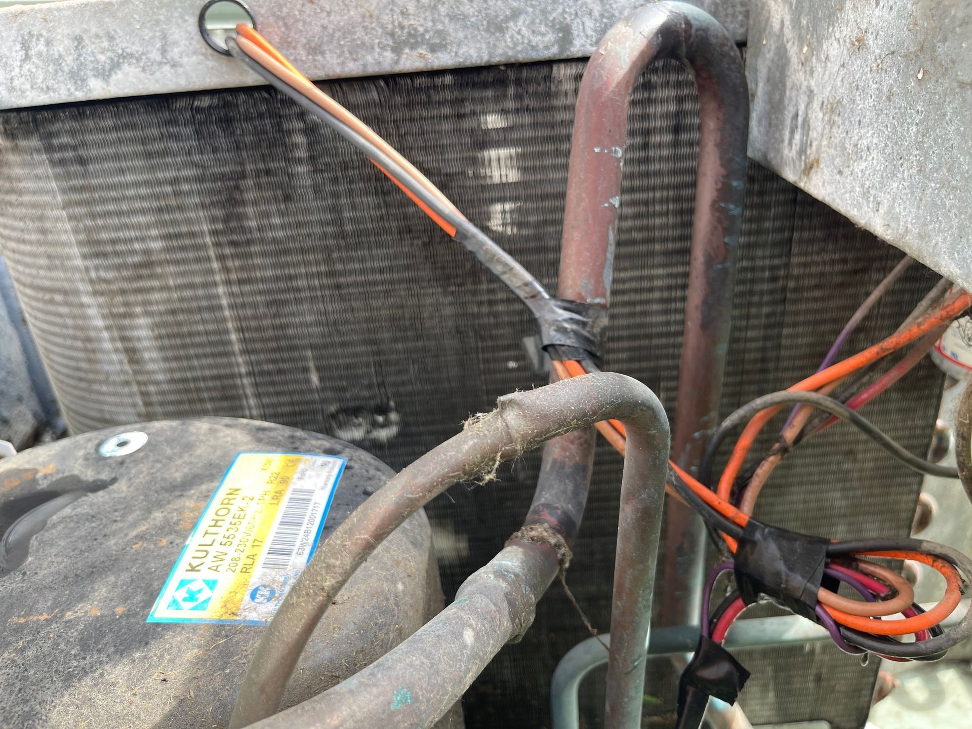 Close-up of an air conditioner's internal components: copper tubes, wires, and compressor, possibly showing damage.