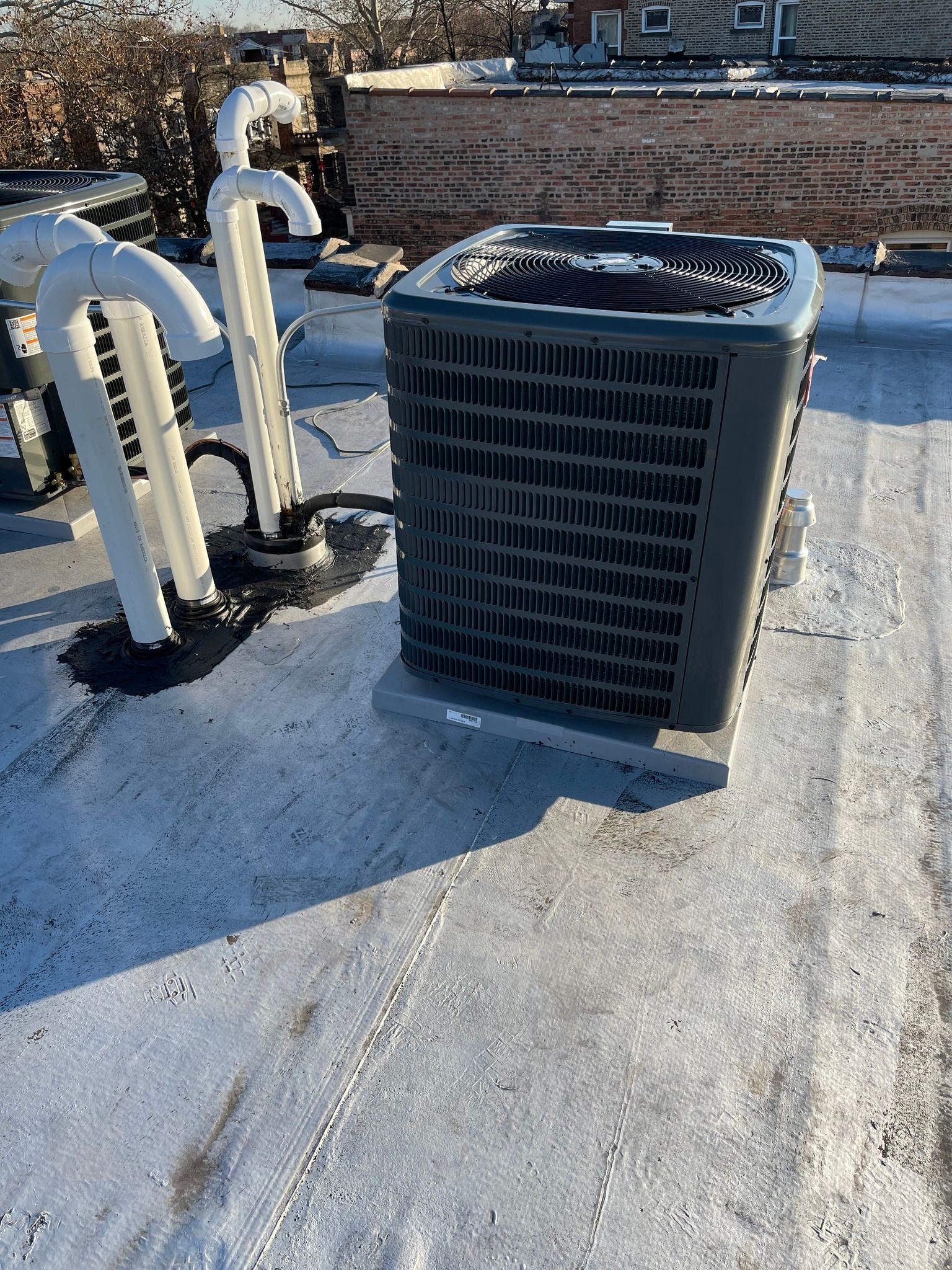 HVAC unit on a rooftop with white pipes; gray and white roof, sunlight.
