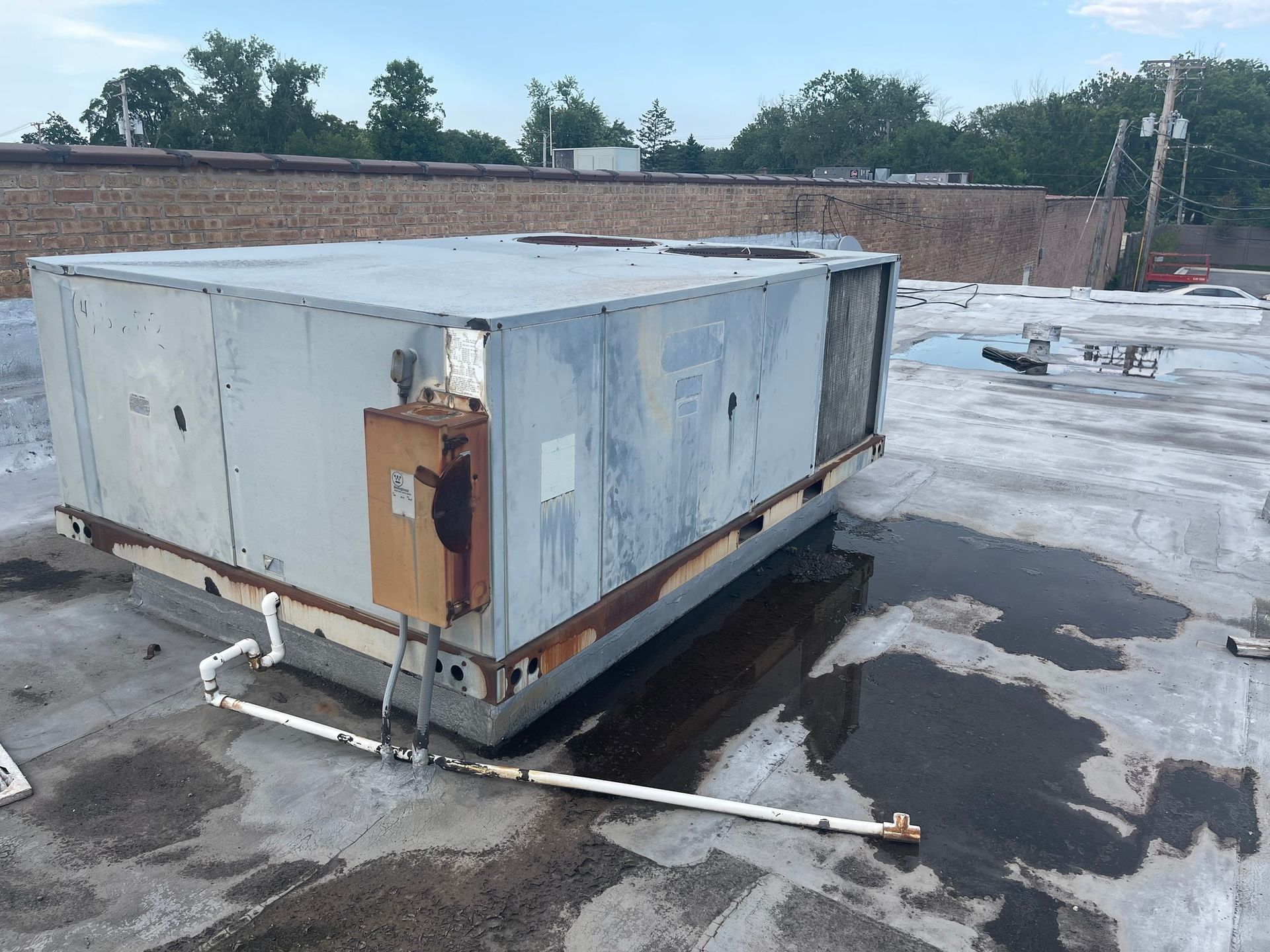 A large, weathered HVAC unit on a flat rooftop. Gray, rusty metal with a brown electrical box.