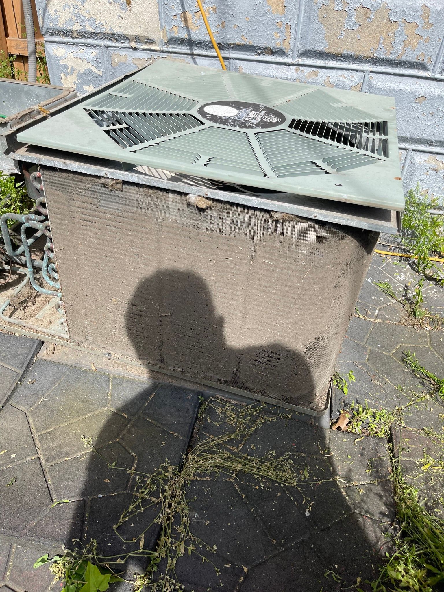 Air conditioner unit with shadow of person on paving stones.