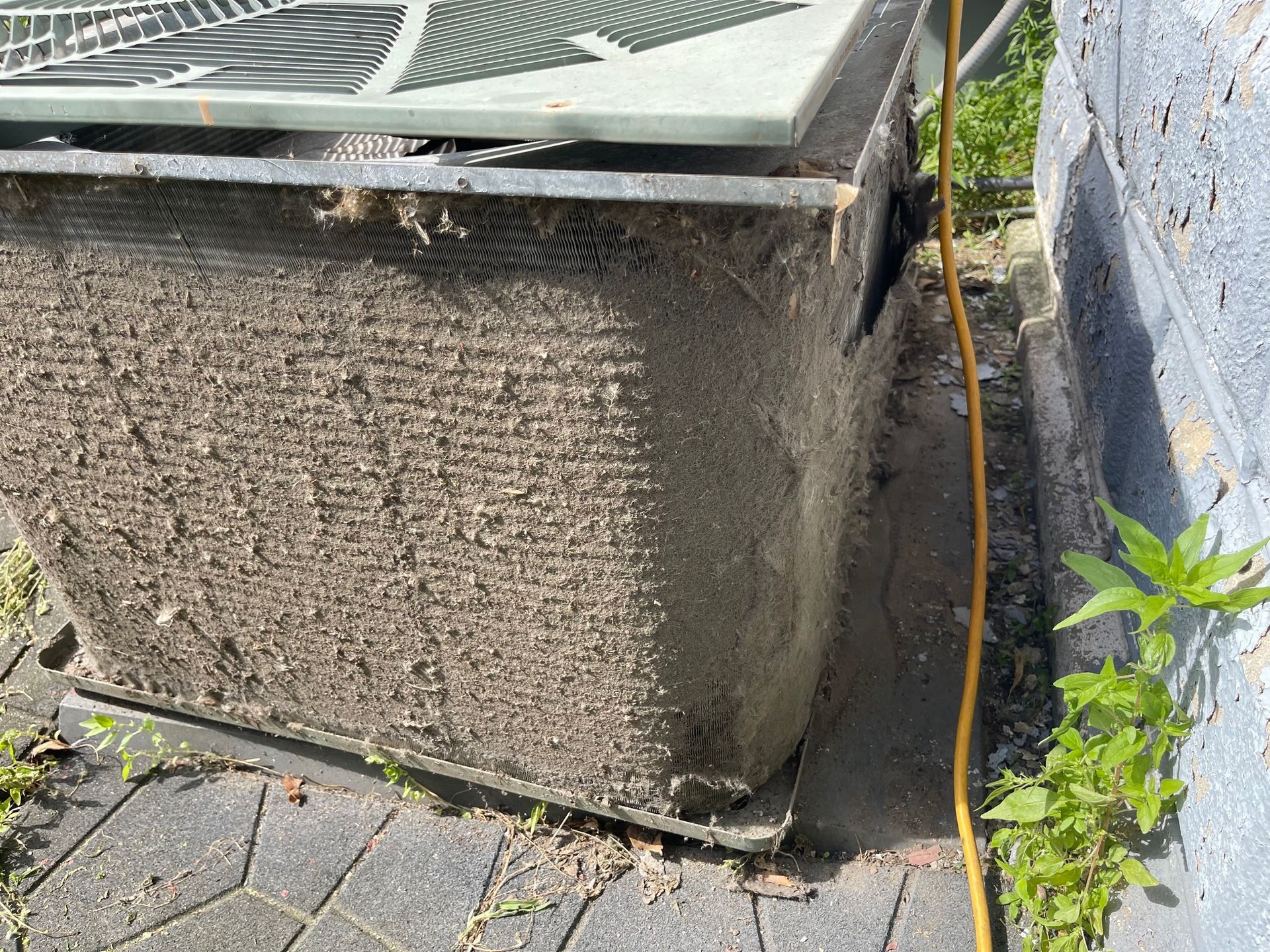 Dusty AC unit, outdoors, beside a wall and sidewalk.