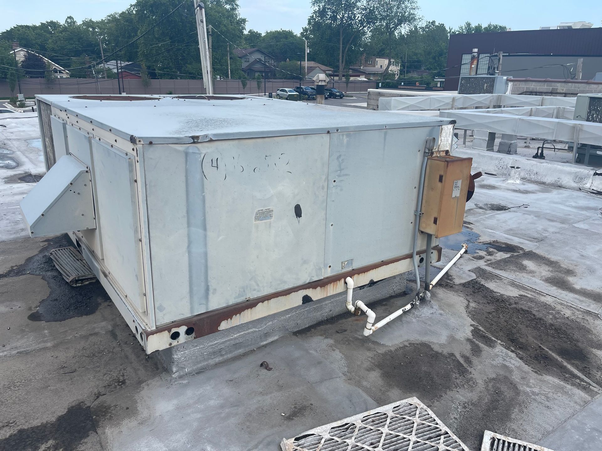 Large, weathered rooftop HVAC unit on a gray flat roof with white pipes and filter.