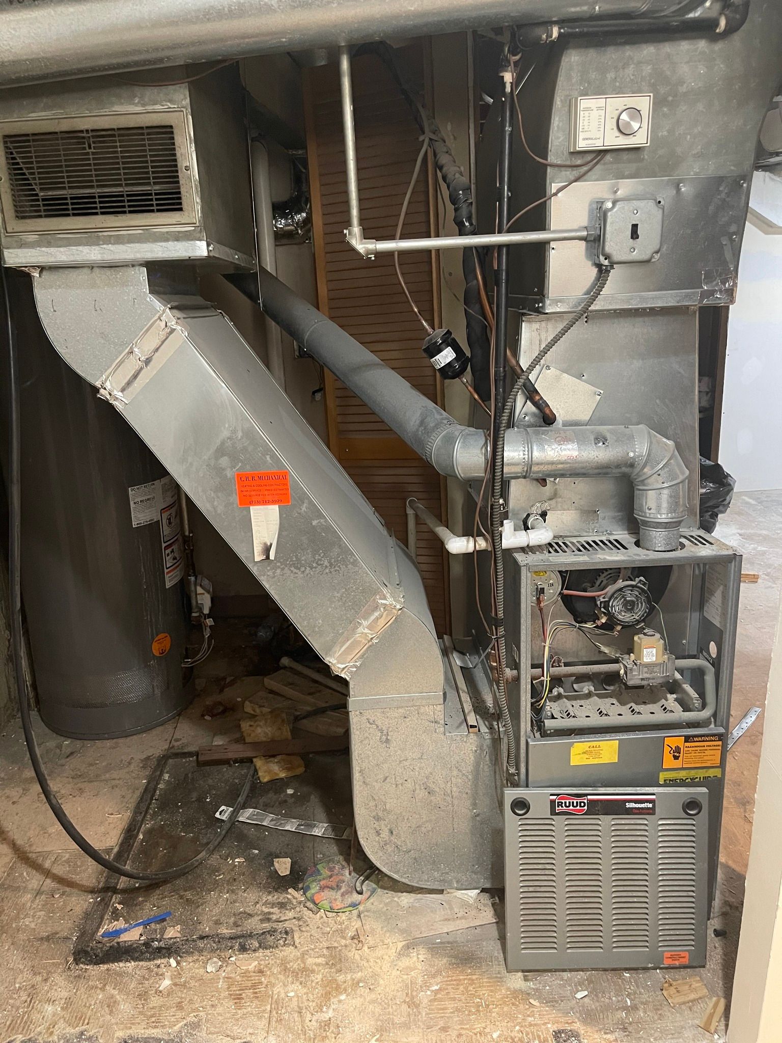 Furnace with ductwork in a utility room. Metal and gray components, warning labels are visible.
