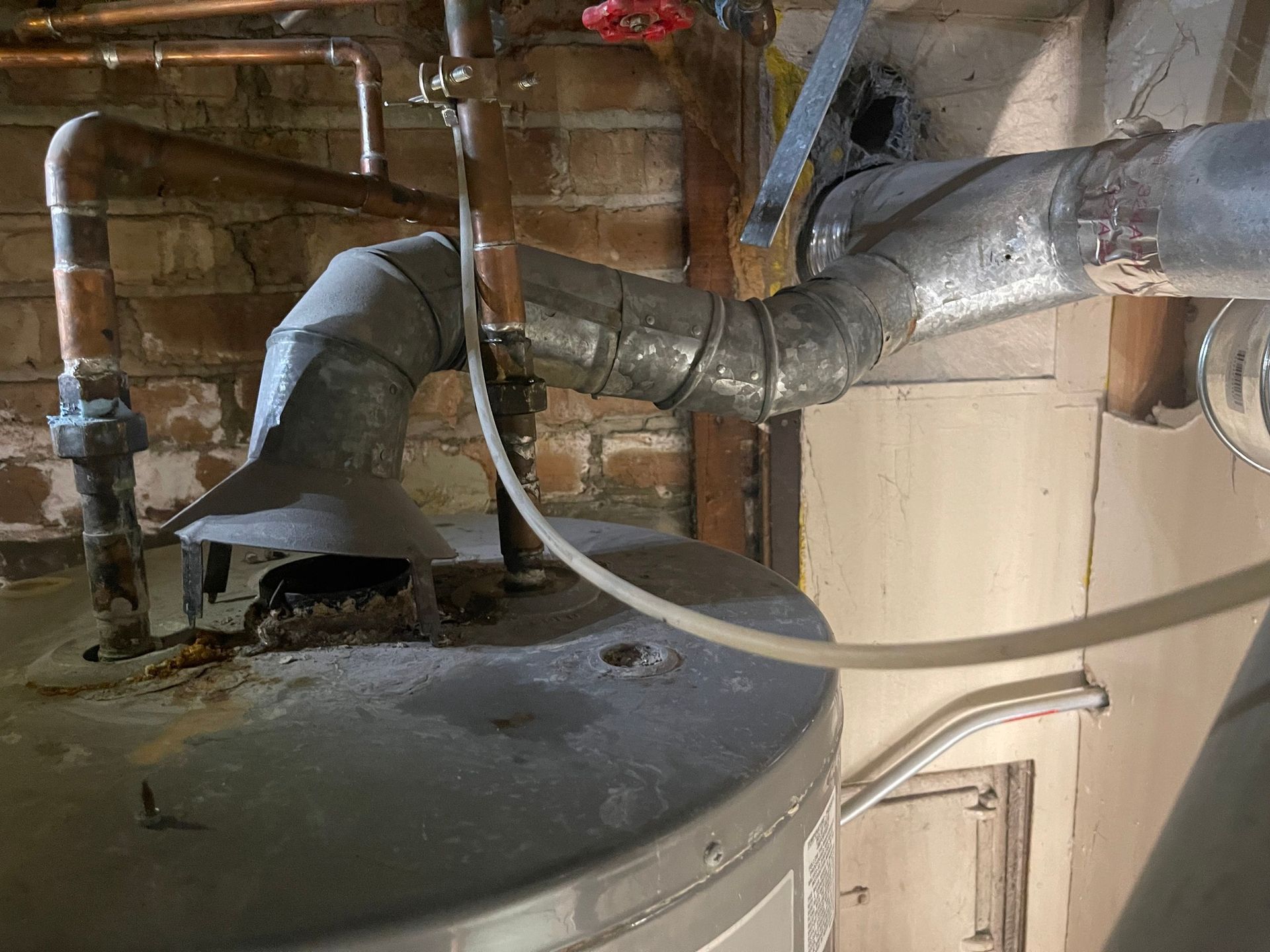 Water heater with vent pipe and copper pipes in a basement setting.