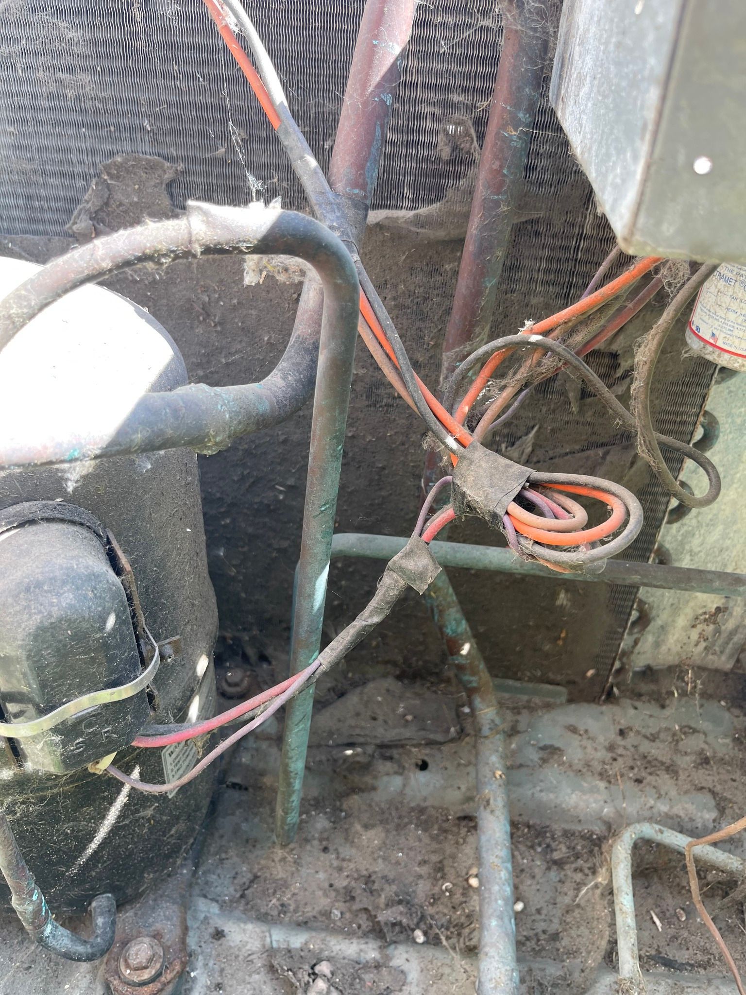 Close-up of a dirty outdoor air conditioning unit with wires, pipes, and compressor.