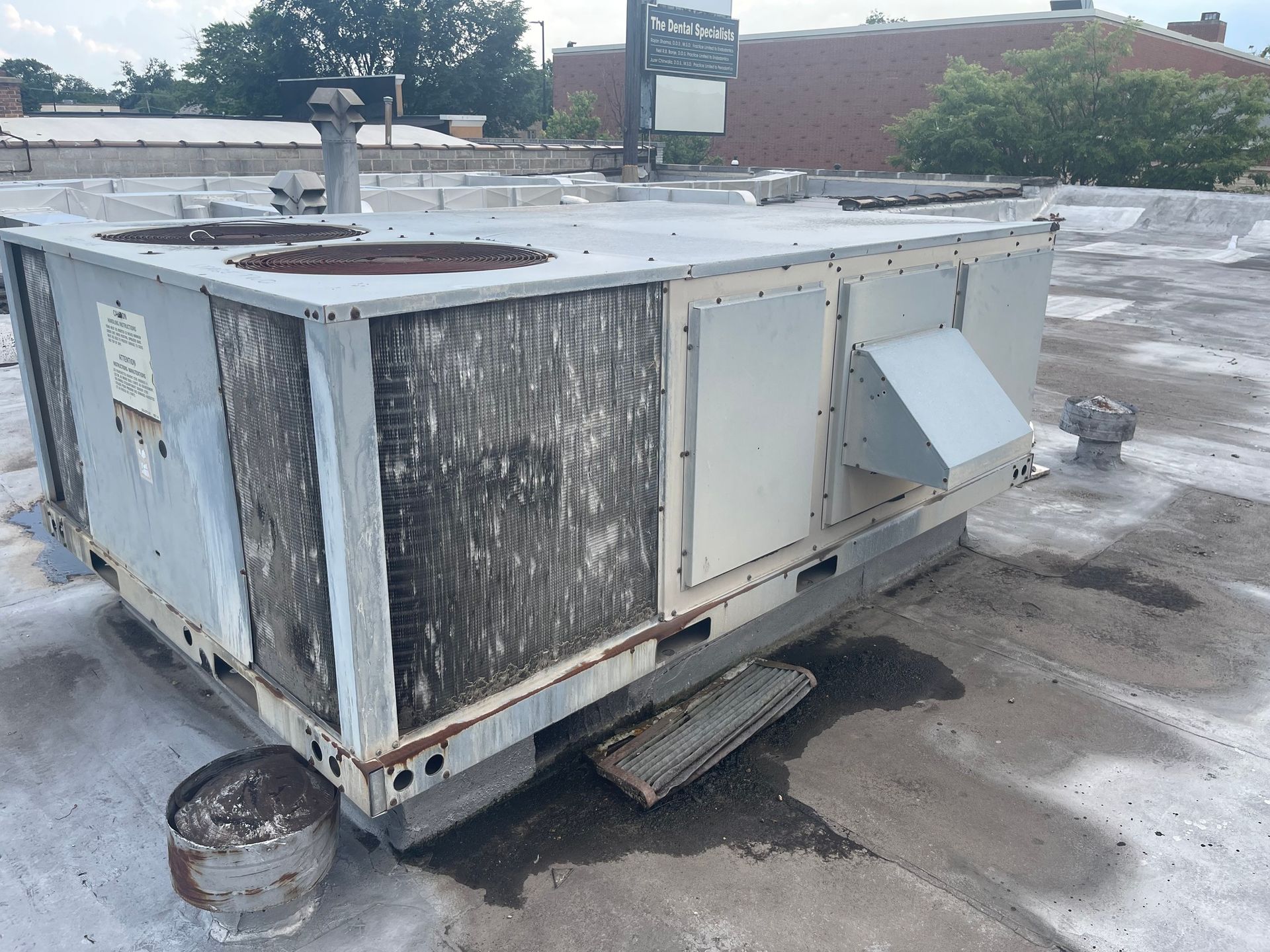 Rooftop HVAC unit, weathered with debris. Gray, metal, on a flat roof.