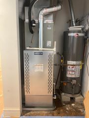Furnace and water heater in a narrow alcove. Silver furnace and grey water heater on concrete blocks.