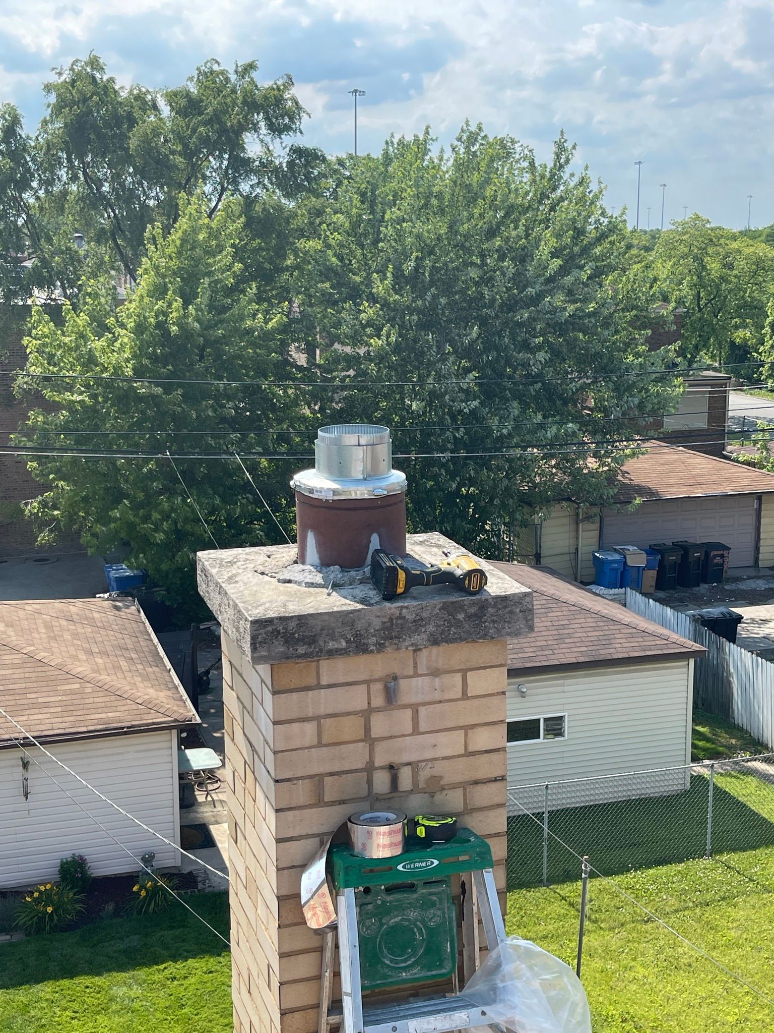 A chimney with a metal cap, tools, and supplies on top, trees in the background.