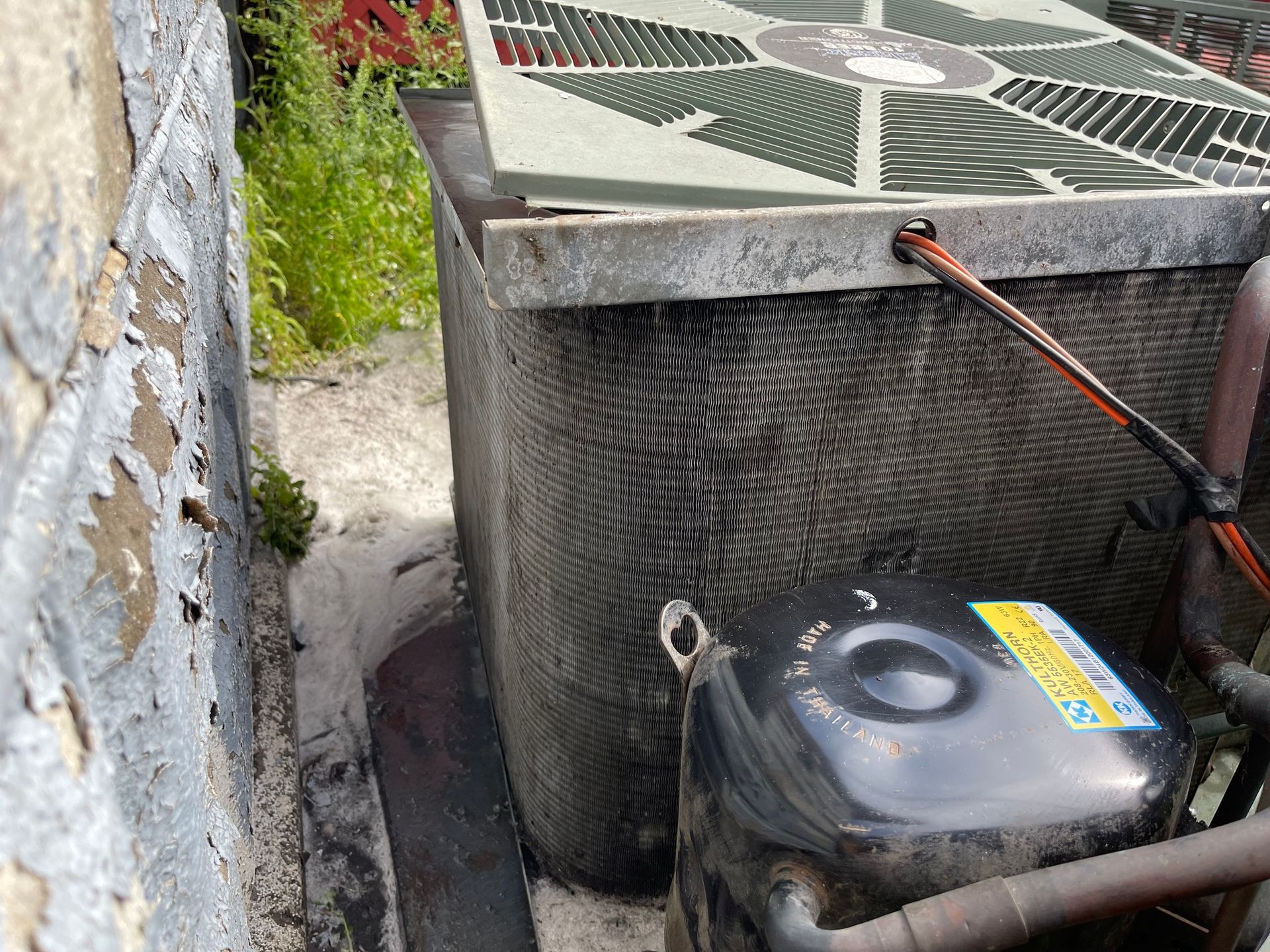 Air conditioner unit near a wall. Gray metal, black compressor, and green grass in the background.