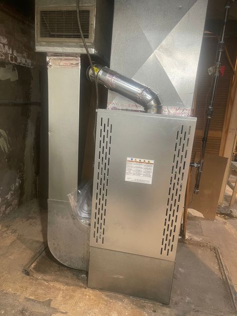 A silver furnace with ductwork in a basement setting.