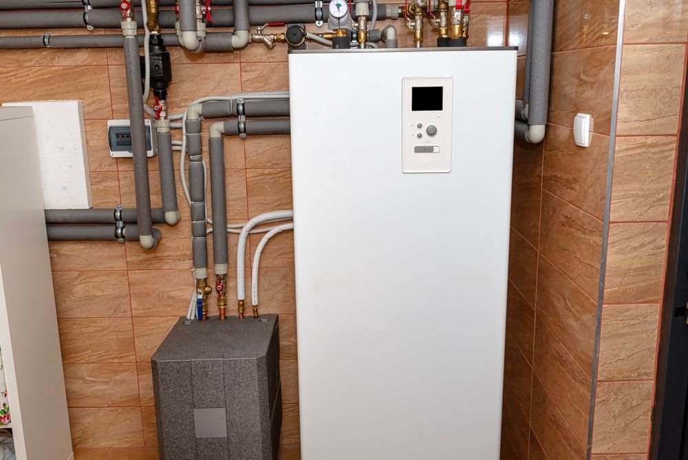 White heating system in a utility room with gray pipes, brown tiled walls, and a small gray box.