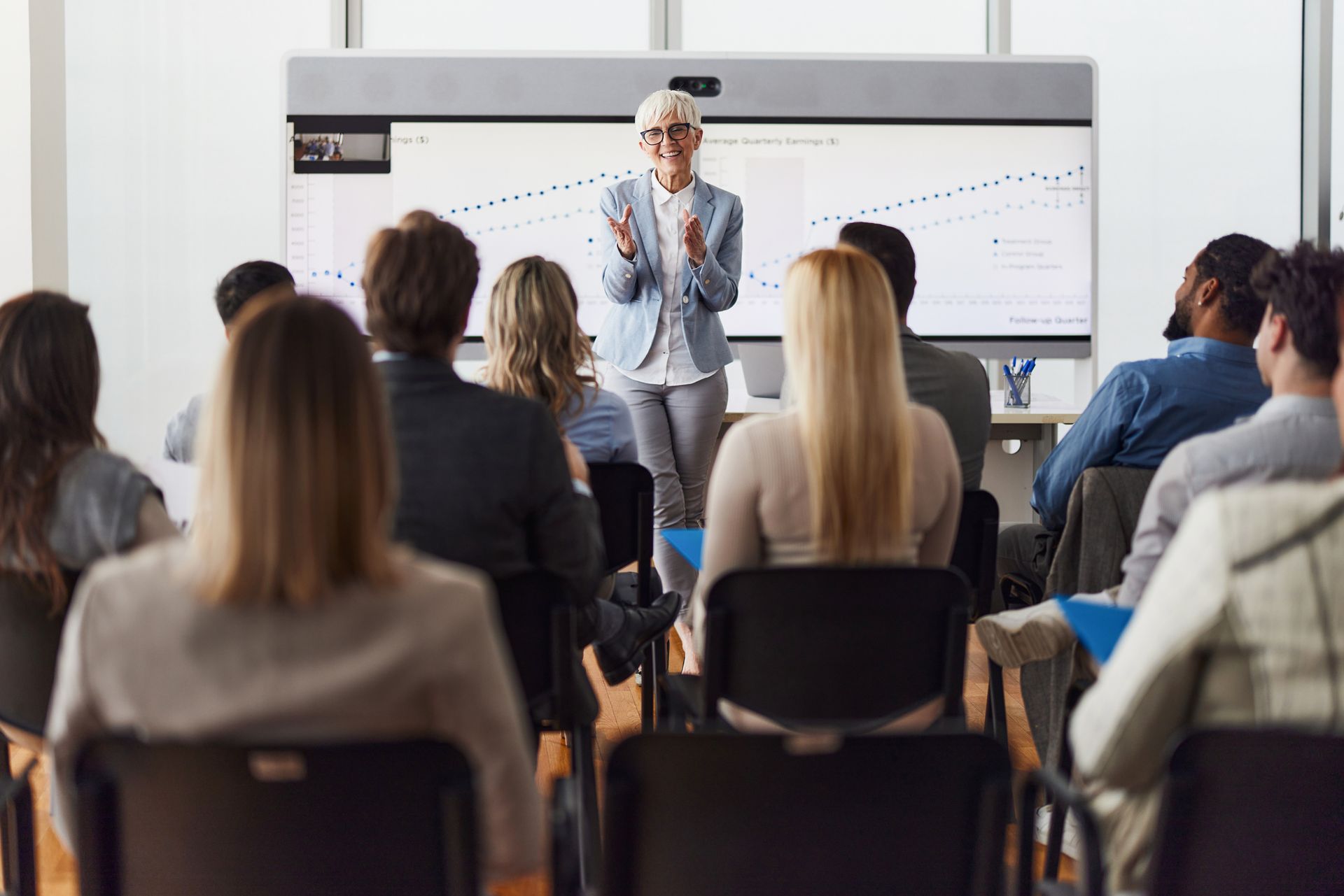 Una donna d'affari tiene una presentazione davanti a un gruppo; sullo schermo è visibile un grafico.