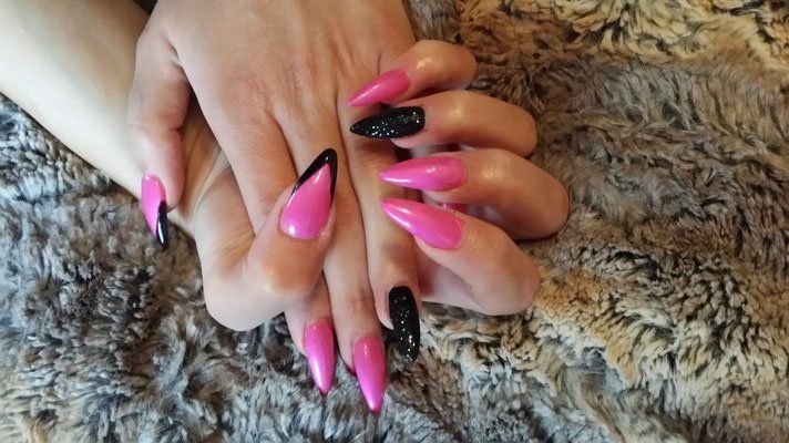 Eine Nahaufnahme der Hände einer Frau mit langen rosa und schwarzen Nägeln.