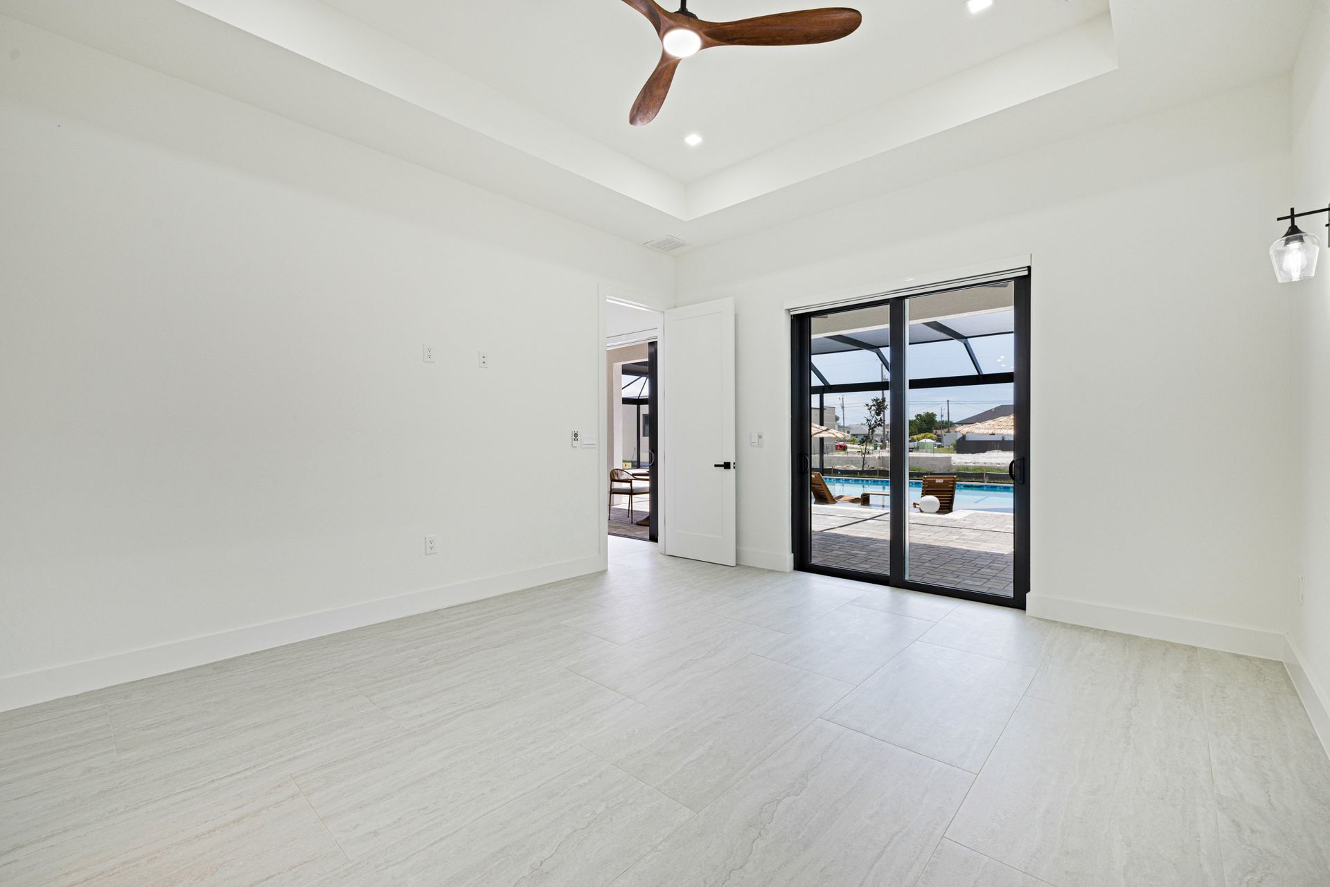 Empty white room with a ceiling fan, sliding glass doors, and bright light.