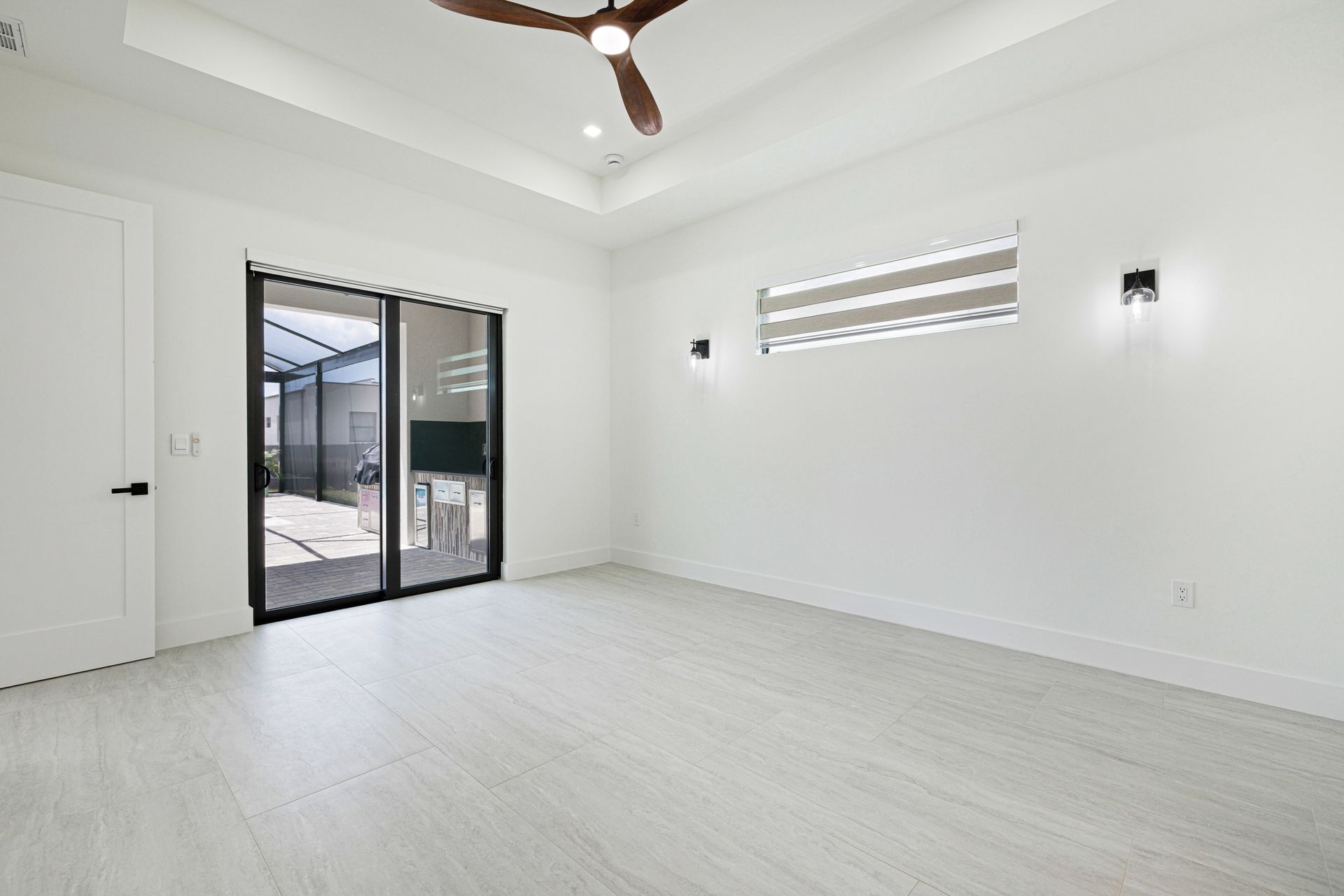 Empty, bright white room with sliding glass doors, ceiling fan, and light-colored flooring.