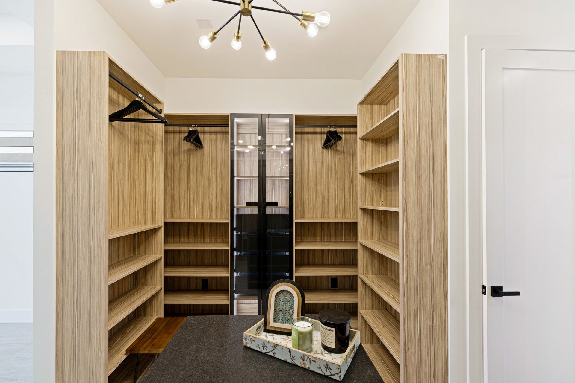 Walk-in closet with wood shelving, black accents, and a central glass cabinet.