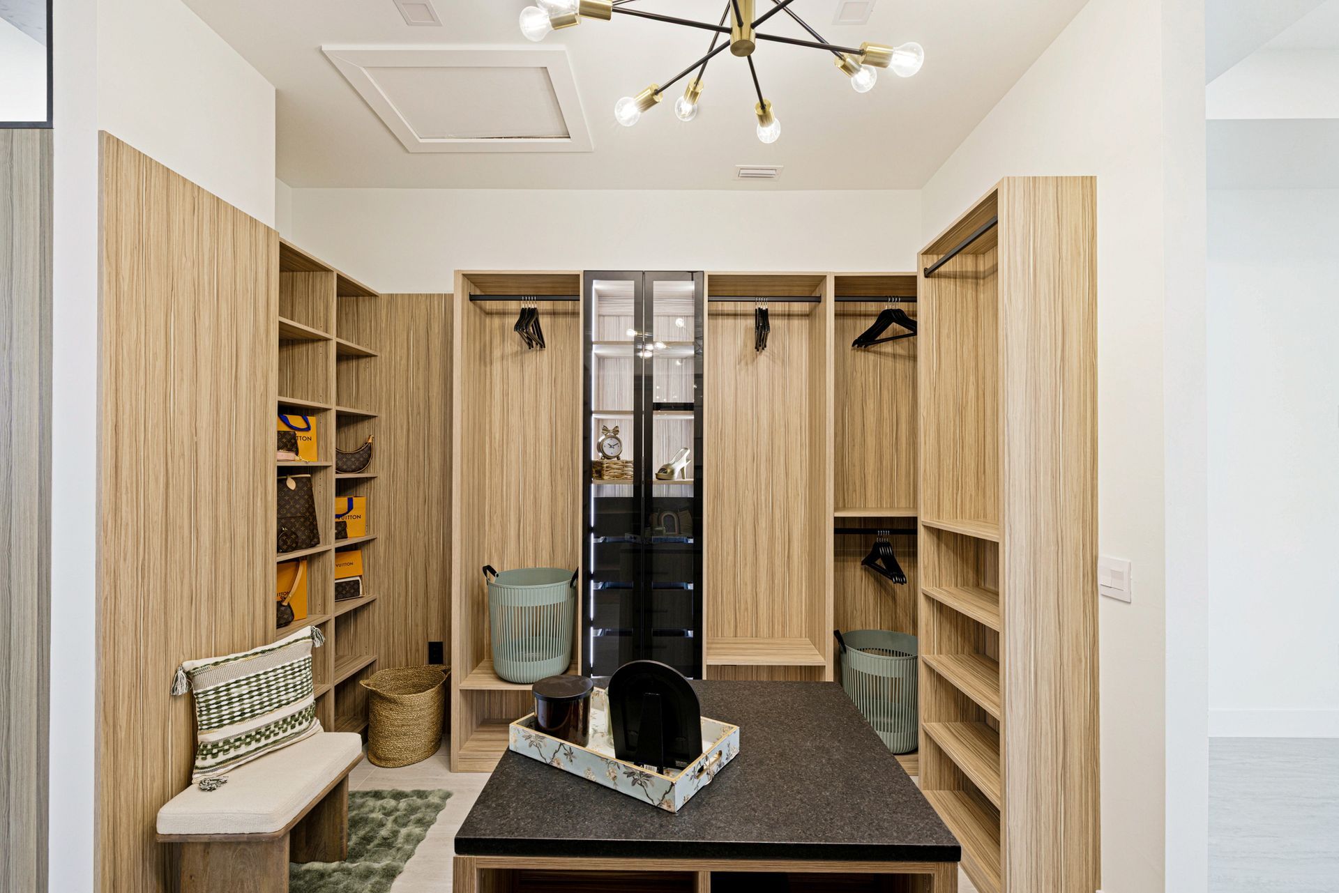 Walk-in closet with wood shelving, clothes, a central island, and a bench seat; a chandelier lights the space.