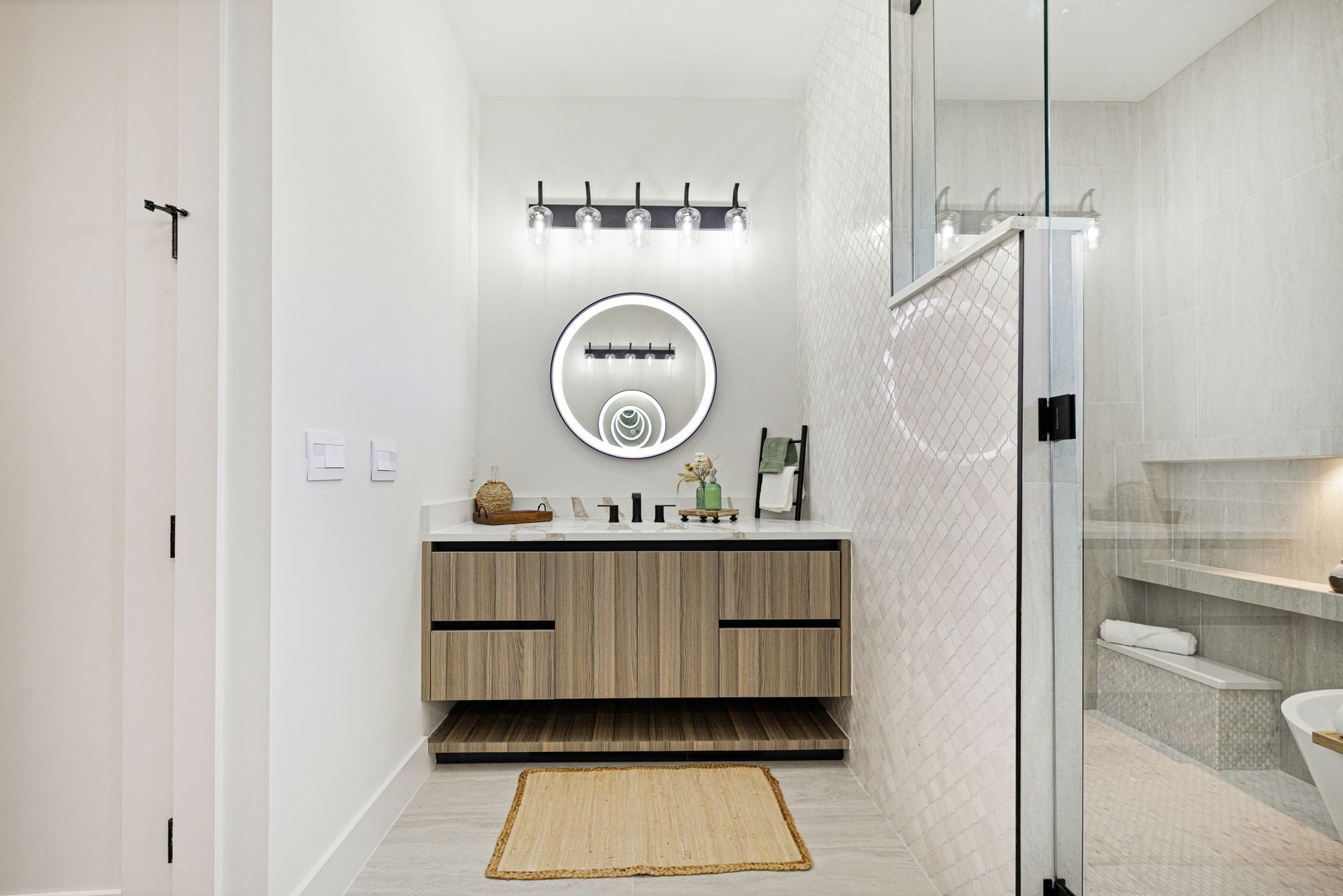 Bathroom with wood vanity, round mirror, and glass shower.