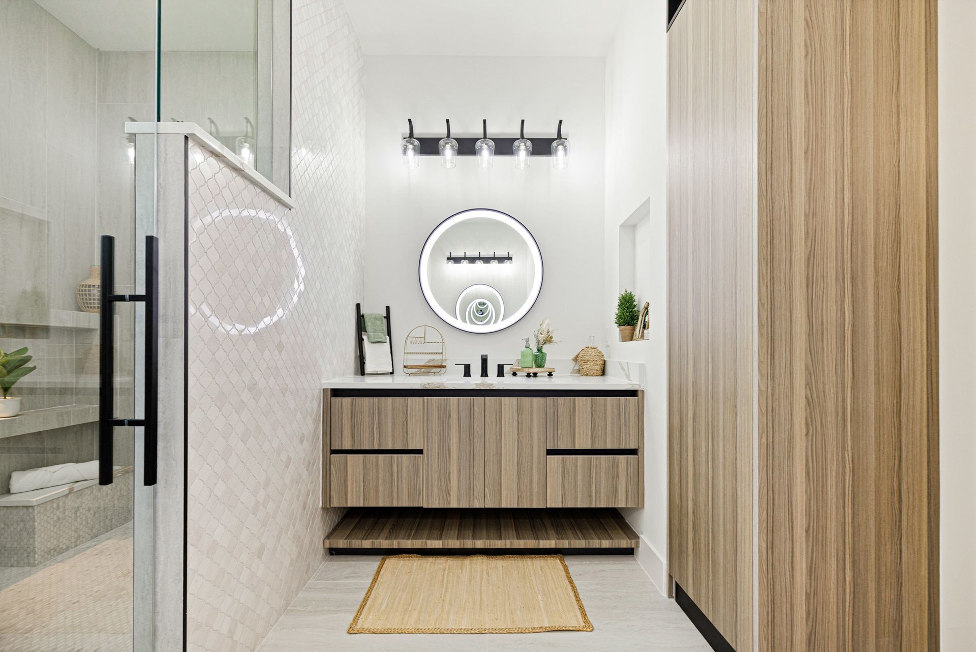 Modern bathroom with wood vanity, round mirror, and glass shower.