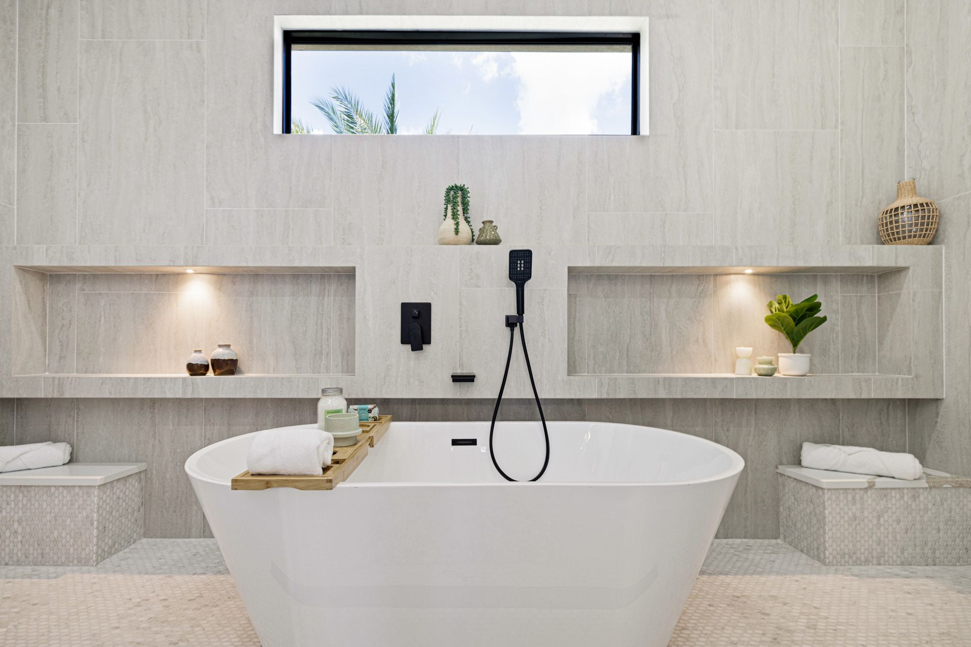 Modern bathroom with a white freestanding tub, built-in shelves, and a window above.