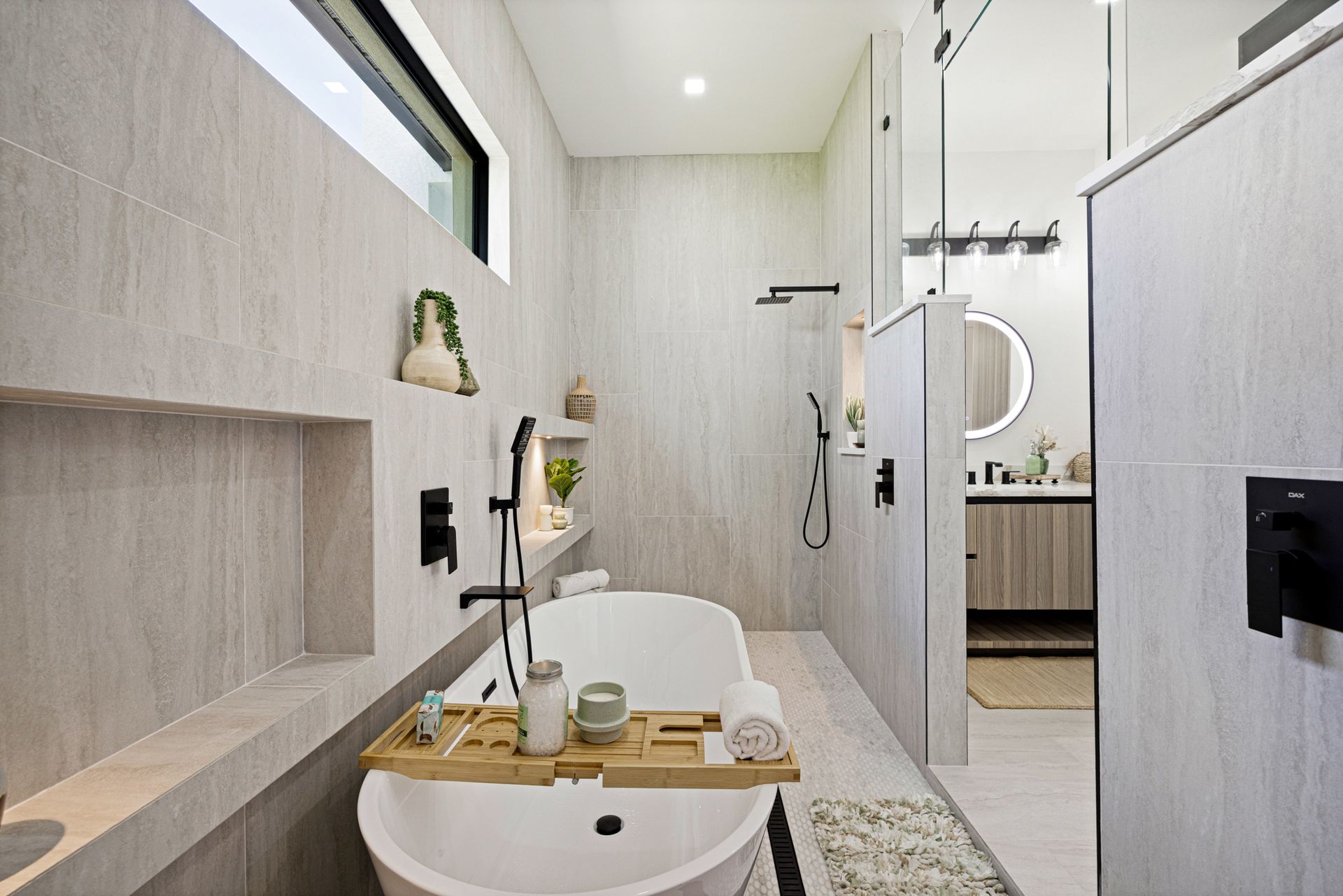 Modern bathroom with a freestanding tub, walk-in shower, neutral tiles, and wood accents.