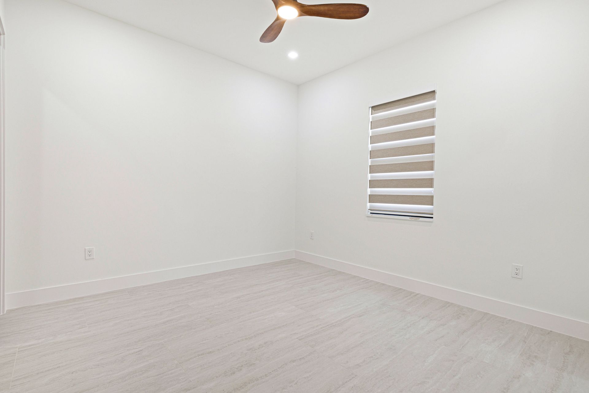 Empty white room with a window, ceiling fan, and light-colored flooring.