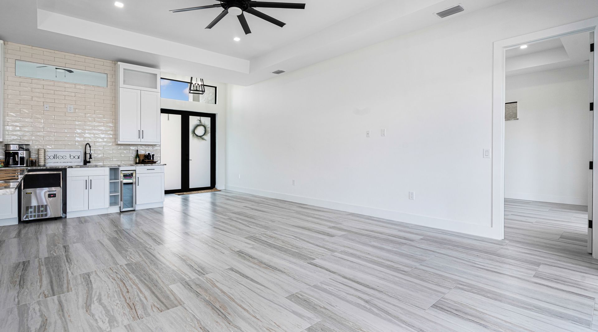 Spacious room with white walls and light wood-look flooring; kitchenette on the left, doorway to the right.