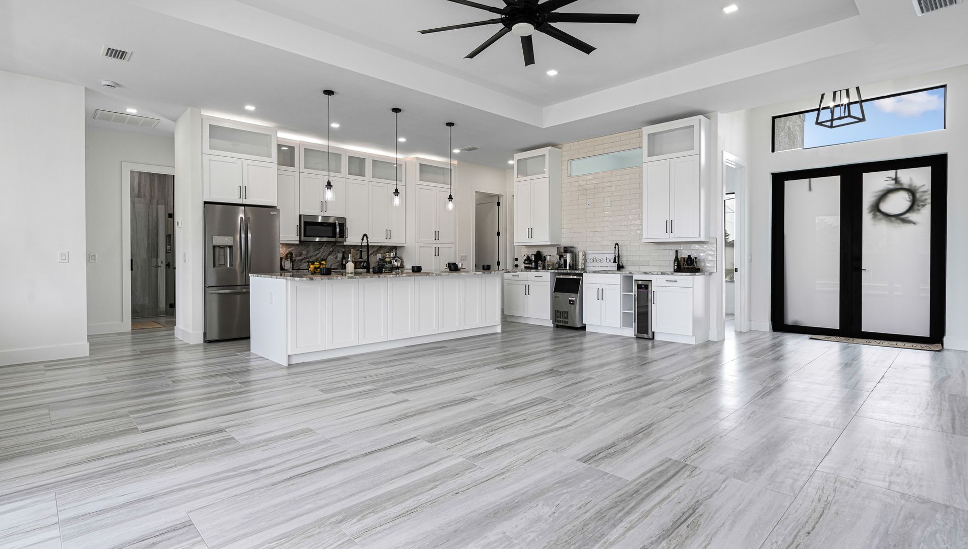 Spacious, modern kitchen with white cabinets, island, stainless steel appliances, and pale gray flooring.