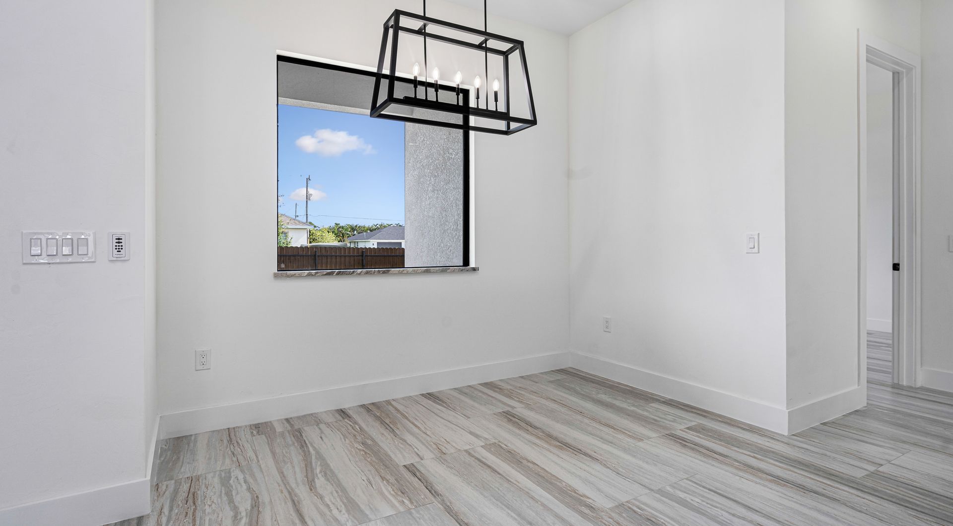Empty dining room with wood-look floors, window, and black chandelier.