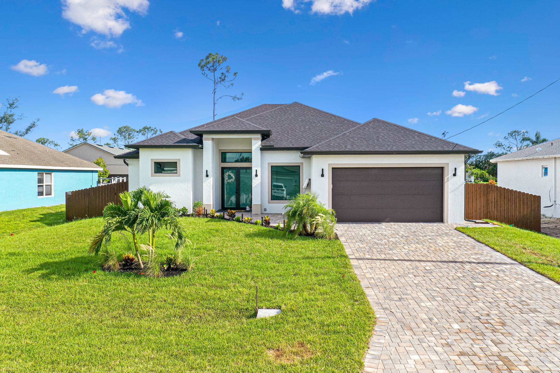 A modern, single-story home with a brown garage door, light exterior, and a green lawn under a blue sky.