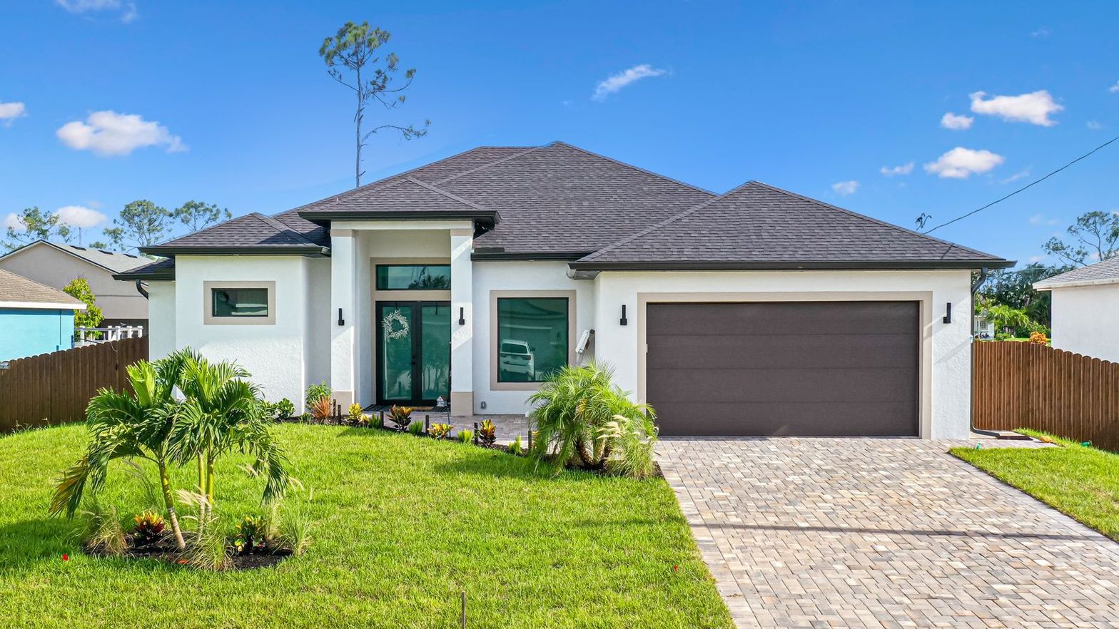 Modern white house with brown roof and garage door; green lawn and blue sky.