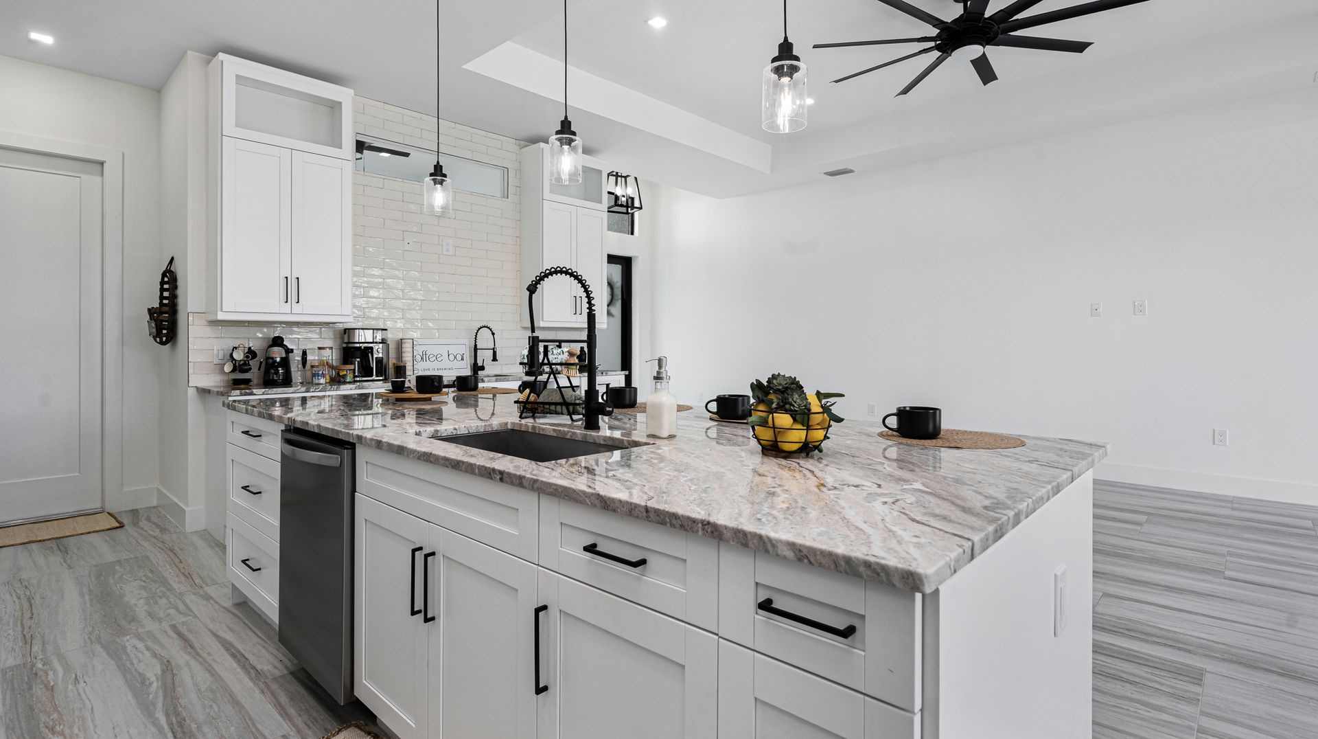 Modern white kitchen with island, stainless appliances, and black fixtures.