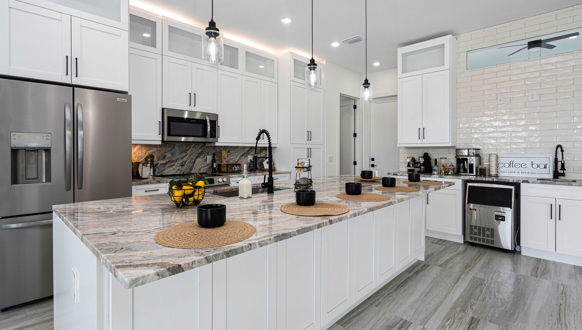Modern white kitchen with granite island, stainless steel appliances, and wood-look floors.