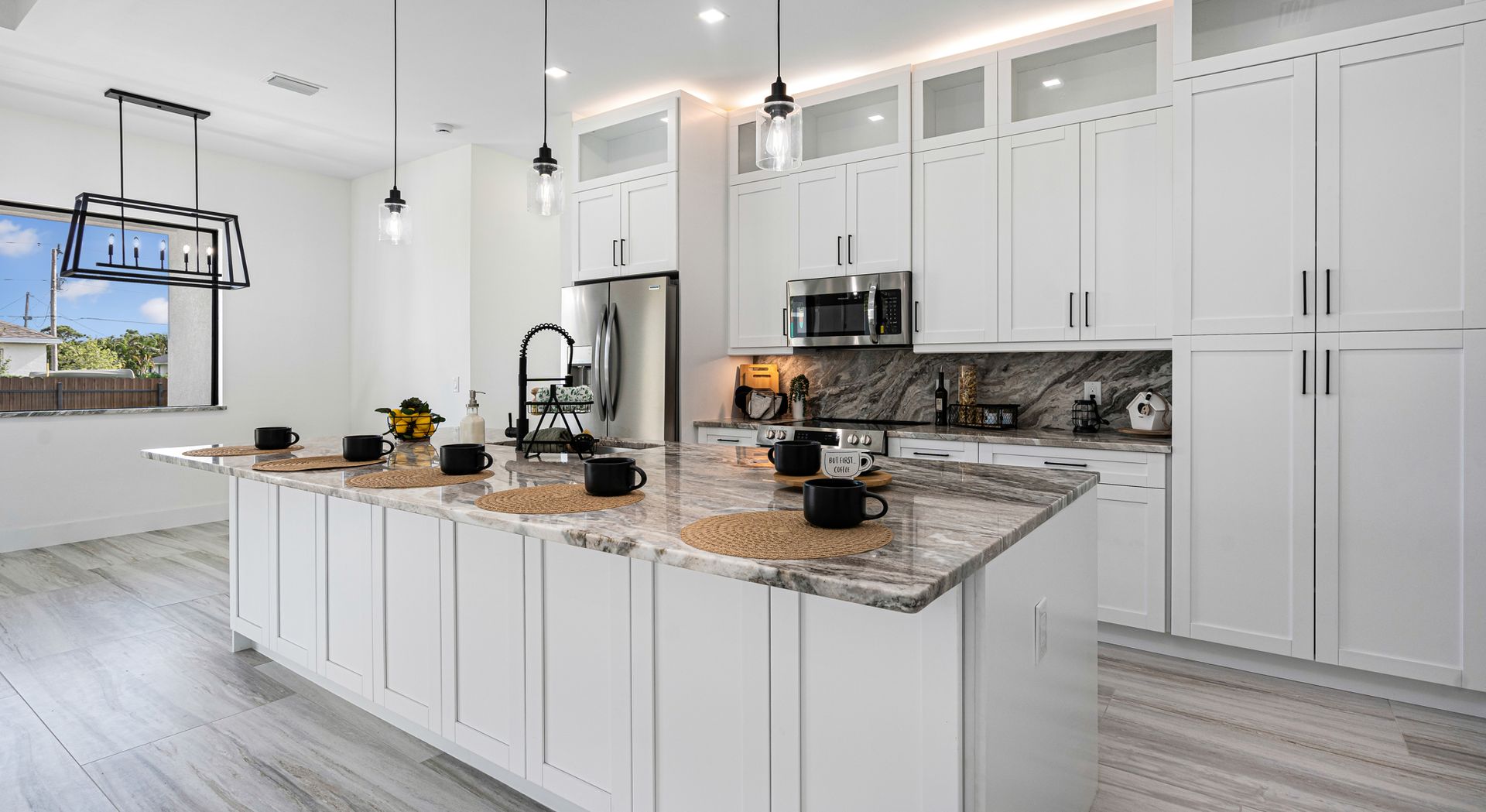 Modern white kitchen with island, countertops, appliances, and lighting.
