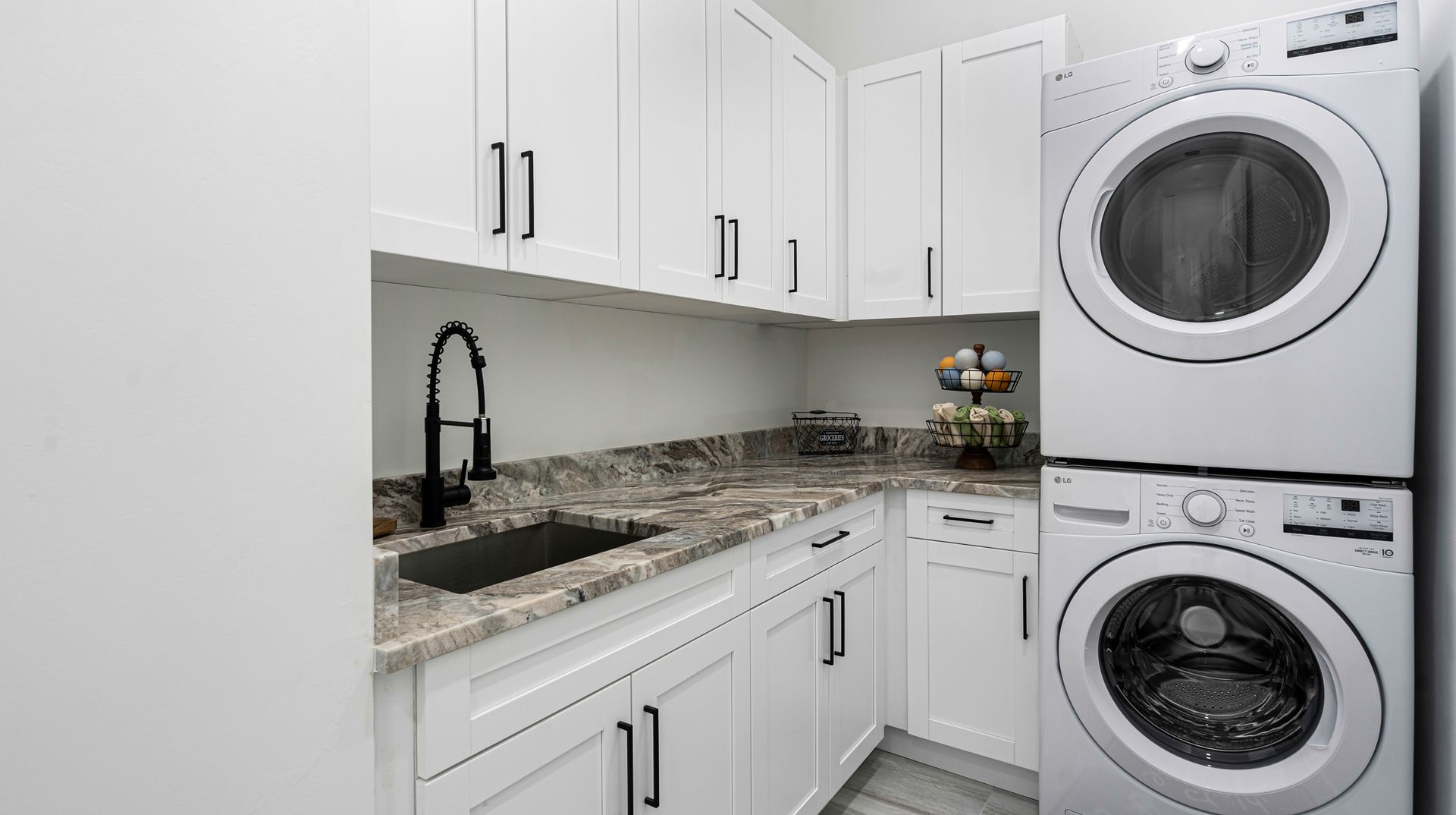 White laundry room with stacked washer/dryer, cabinets, and a sink.