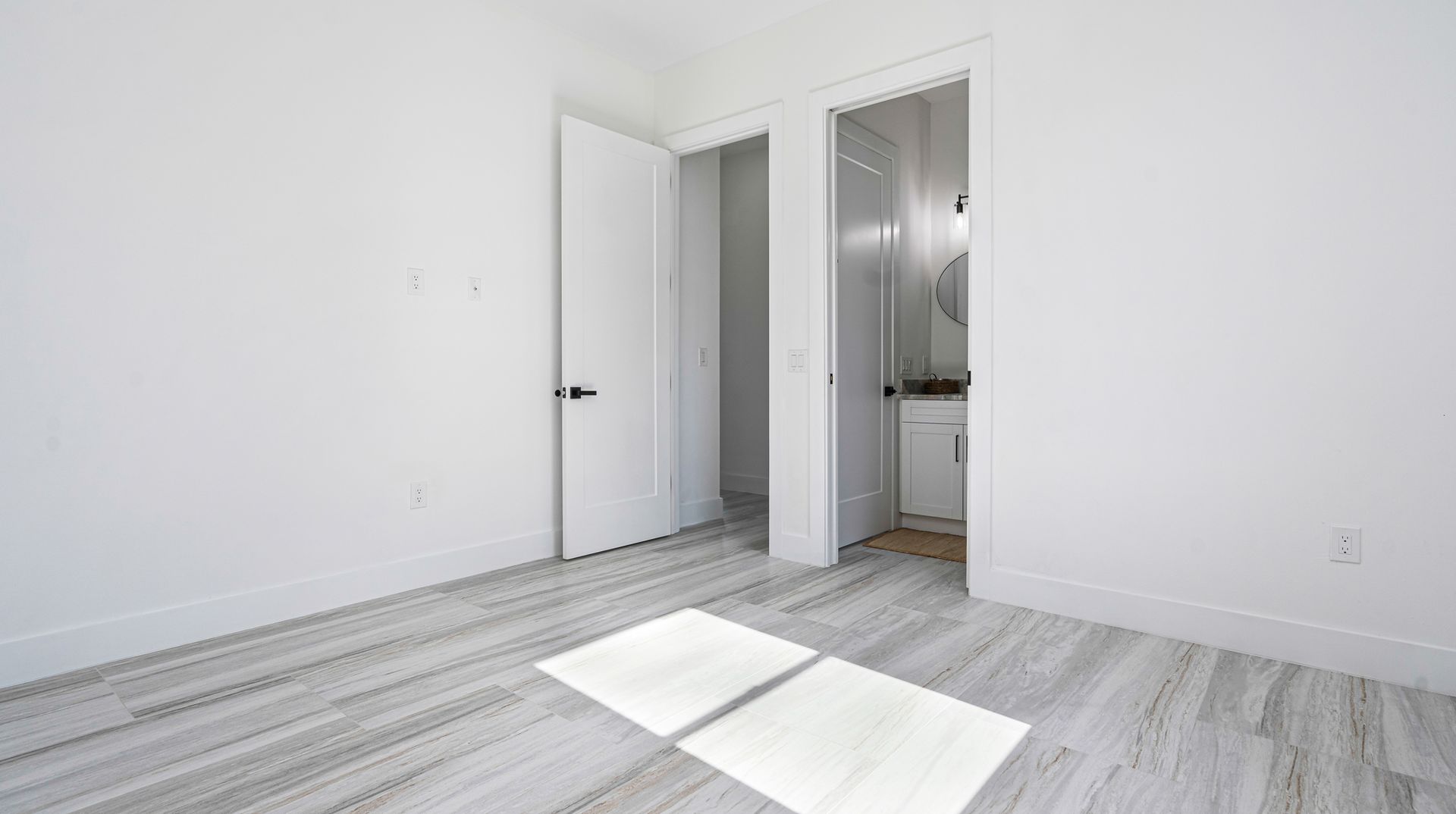 Empty room with light gray wood-look flooring, white walls, and two open white doors.