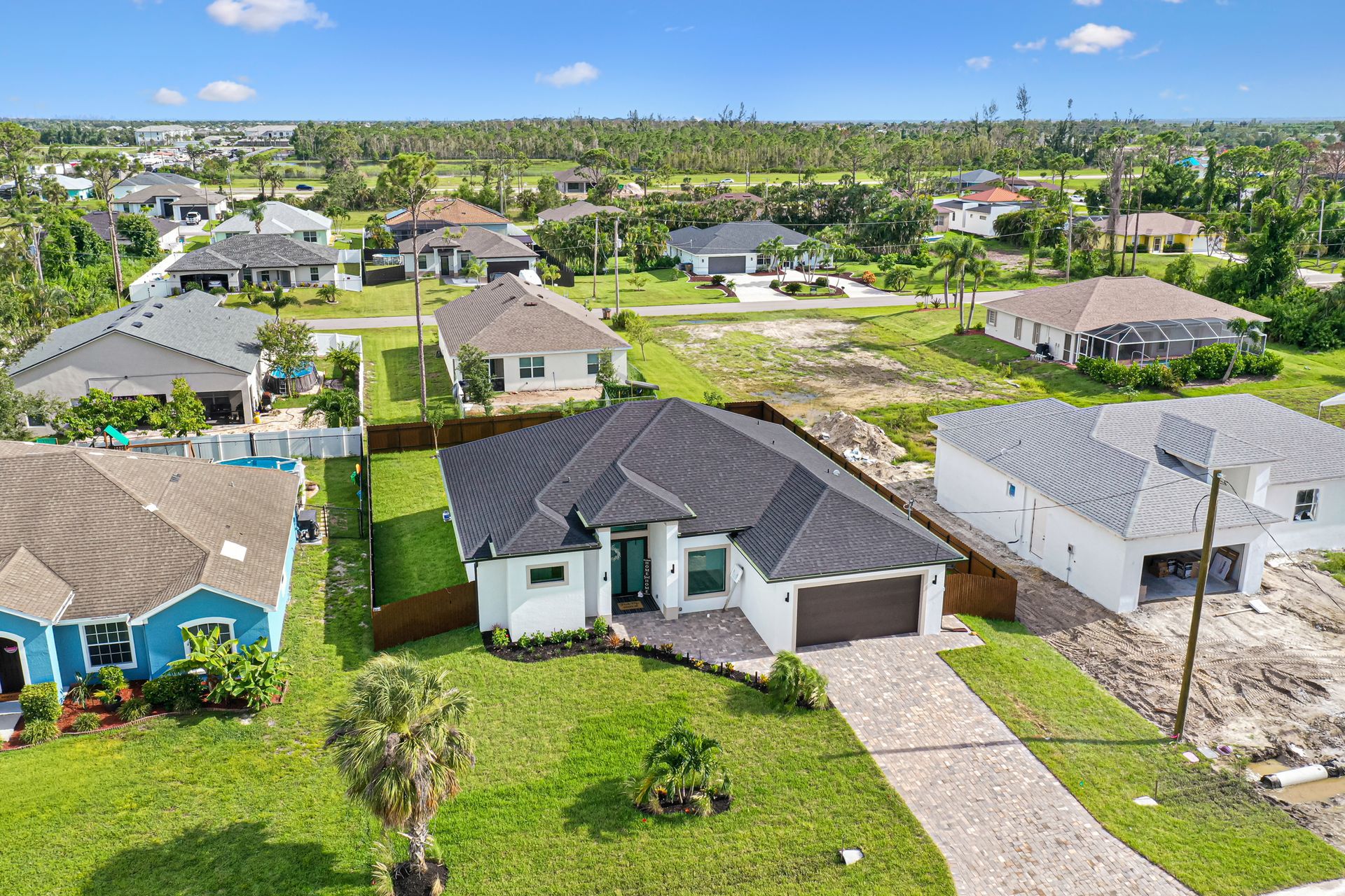 Aerial view of suburban homes with green lawns and construction sites under a blue sky.