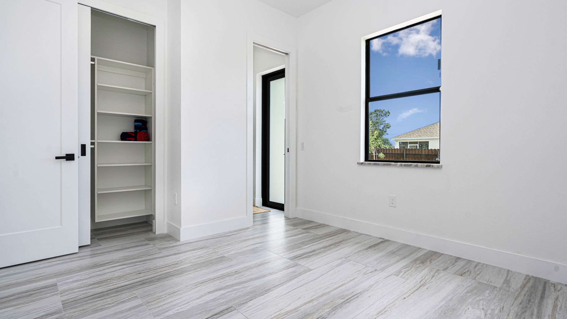 Empty room with white walls, wood floor, open closet, window showing blue sky.