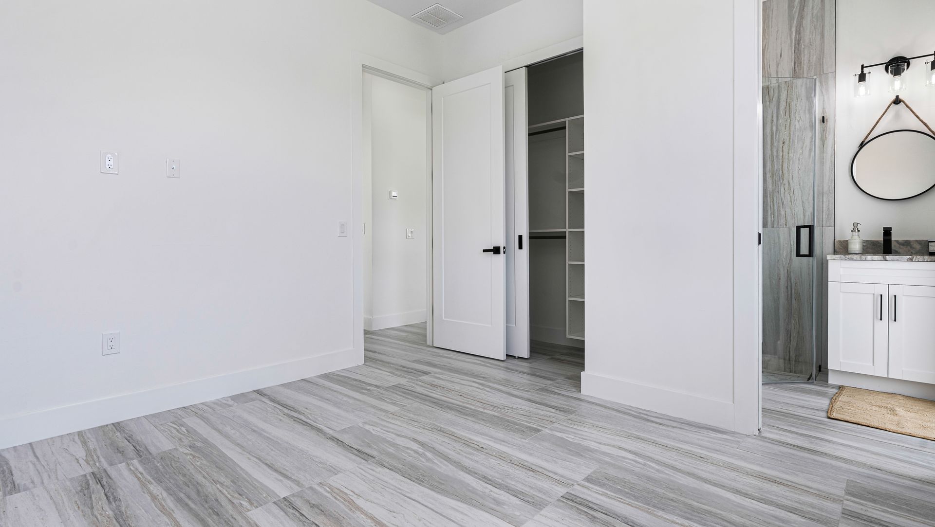Empty bedroom with gray tiled floor, white walls, and open door to a bathroom.