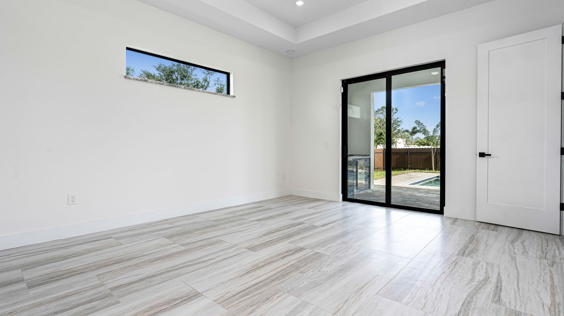 Empty room with light wood-look flooring, white walls, sliding glass door to a patio, and a small window.