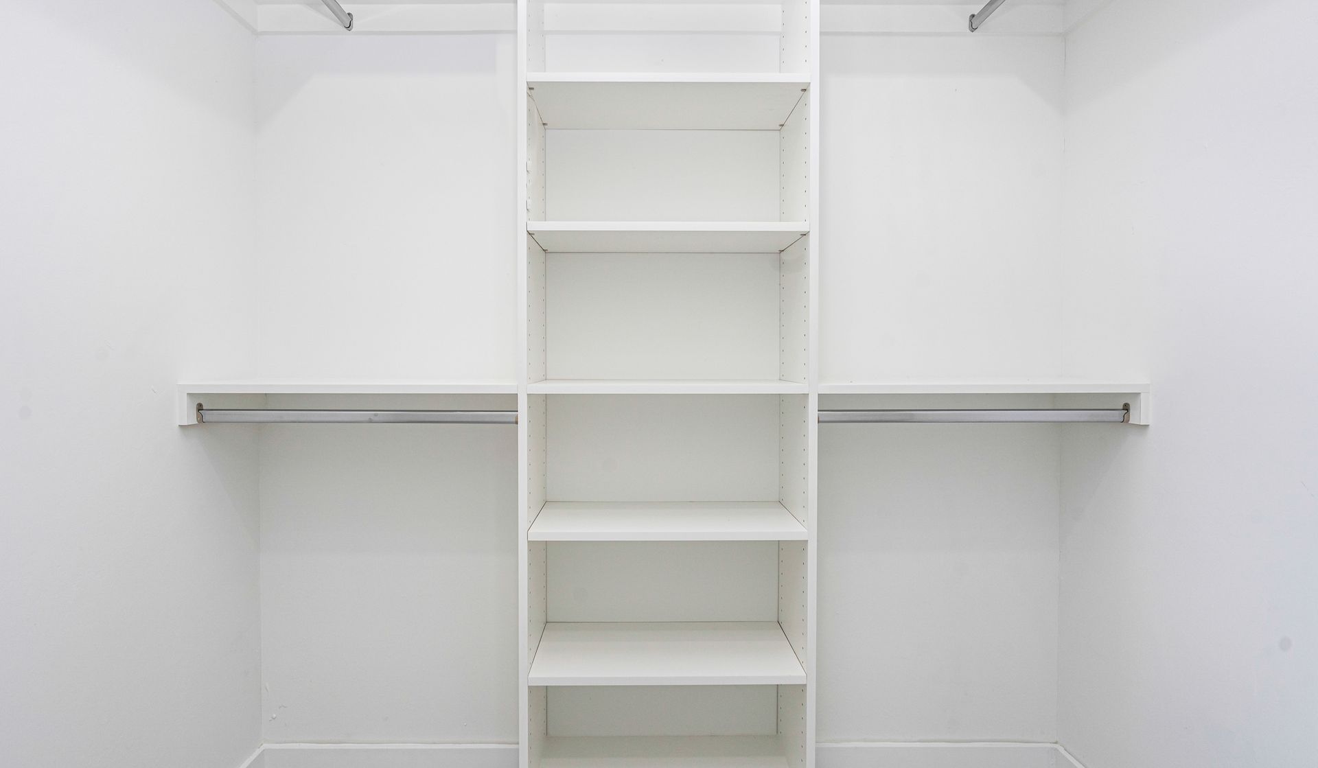 Empty white closet with shelving and two rods for hanging clothes.
