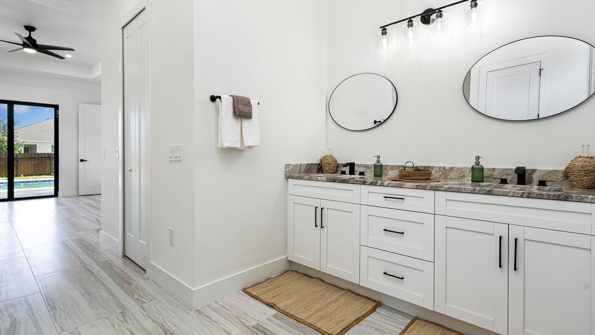 Bright white bathroom with double vanity, two round mirrors, and a door to a patio.