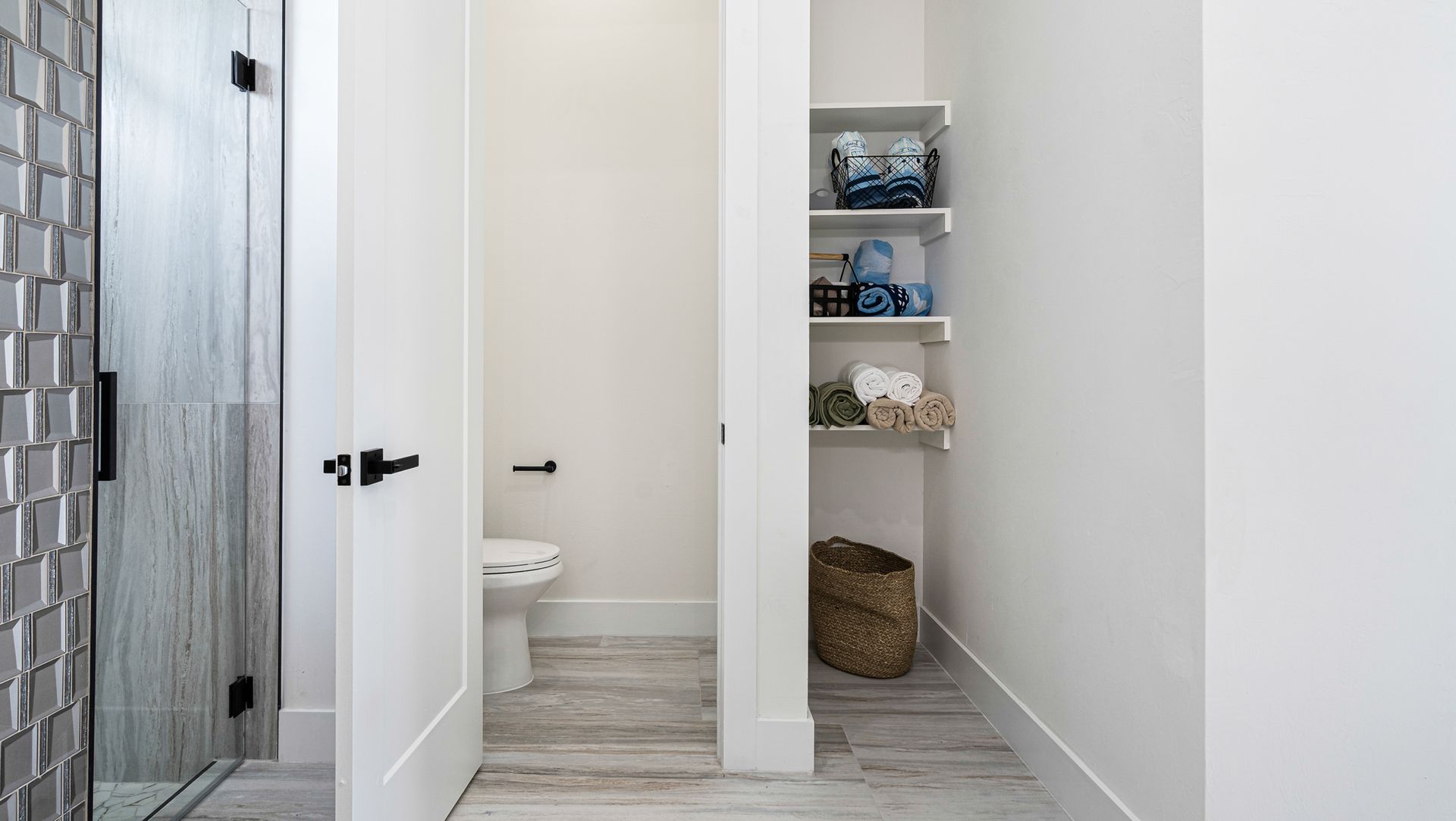 Bathroom with shower, toilet, and storage shelves; light wood flooring.