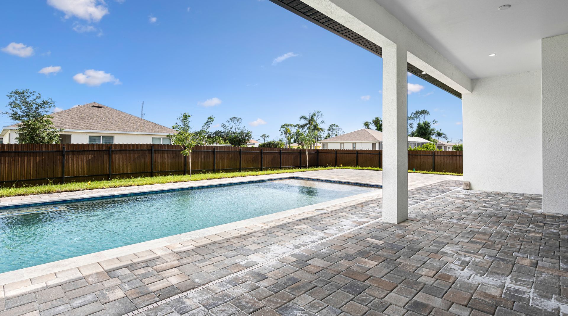 Poolside patio with swimming pool, brick pavers, and a view of houses and blue sky.
