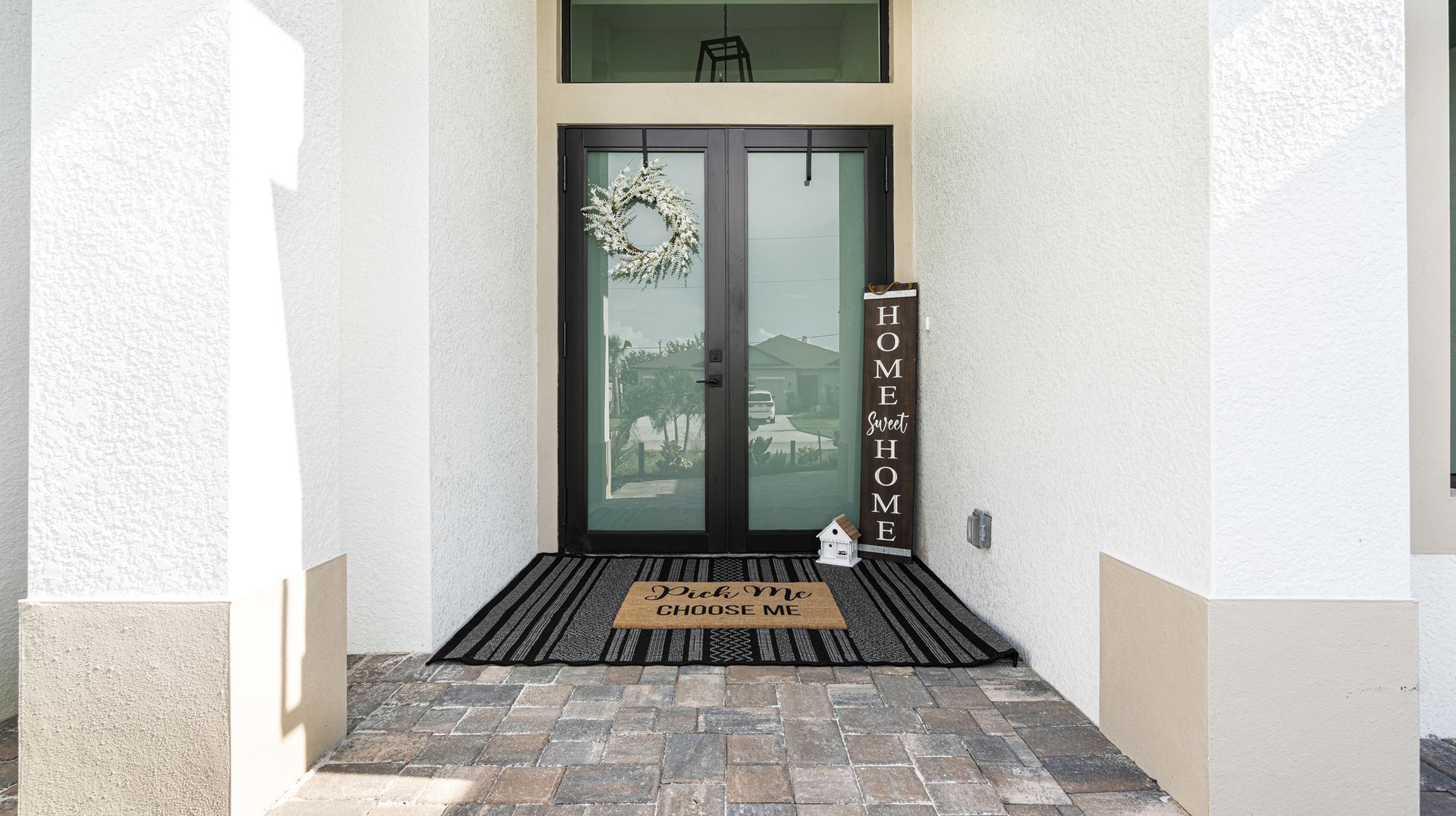 Exterior view of a front door with a wreath and welcome mat in a white-walled space.