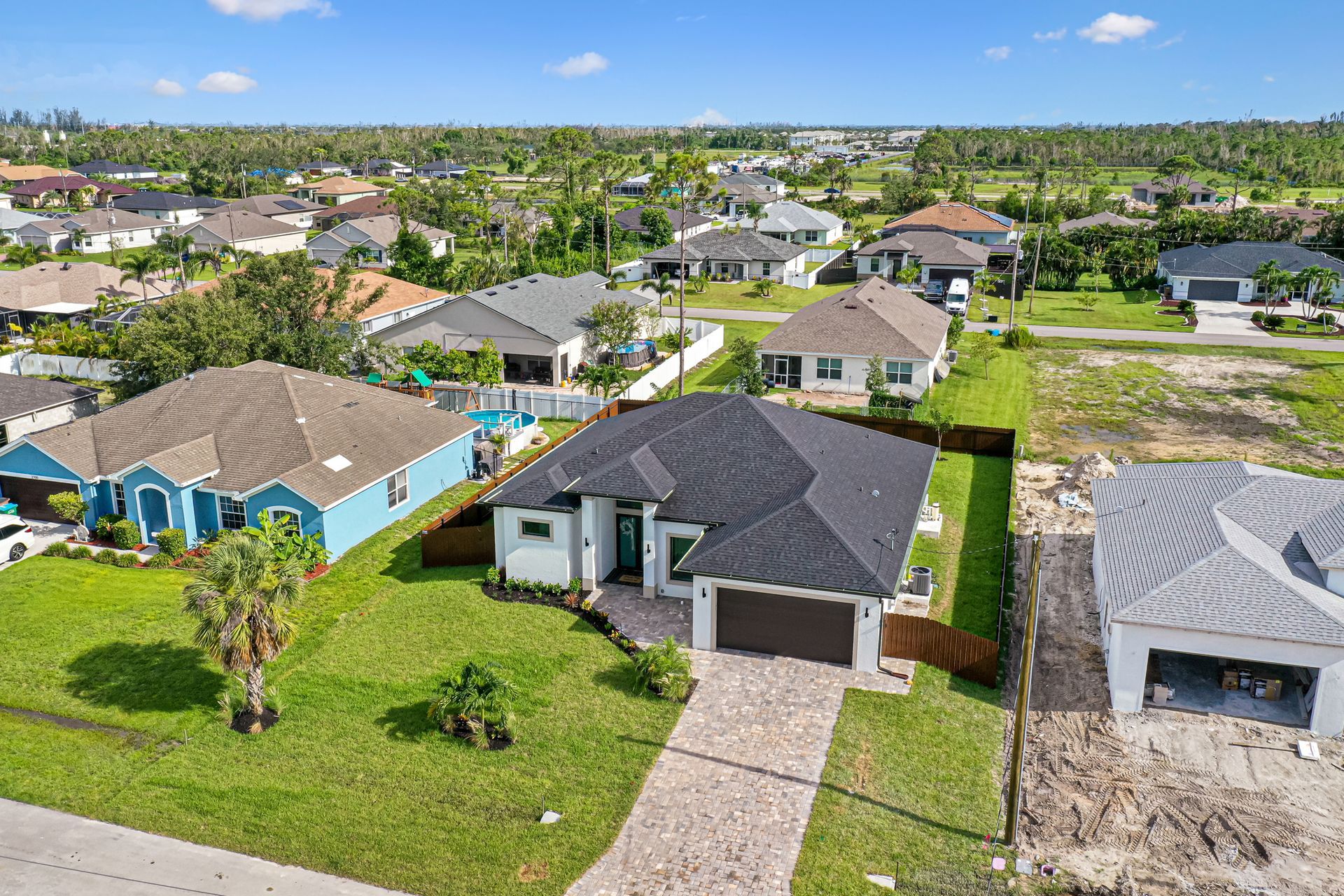 Aerial view of houses in a suburban neighborhood with green lawns, blue skies, and palm trees.