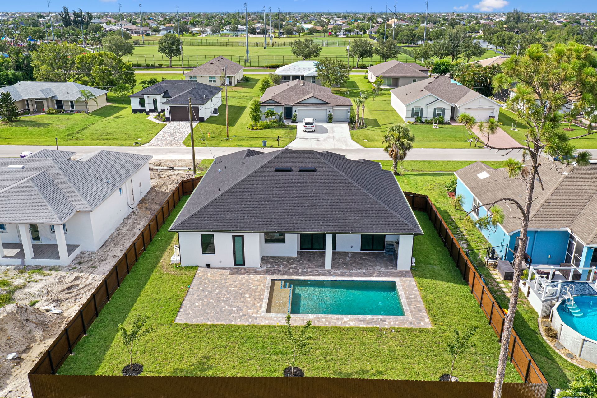Aerial view of a modern home with a pool, surrounded by green lawn and other houses in a suburban neighborhood.